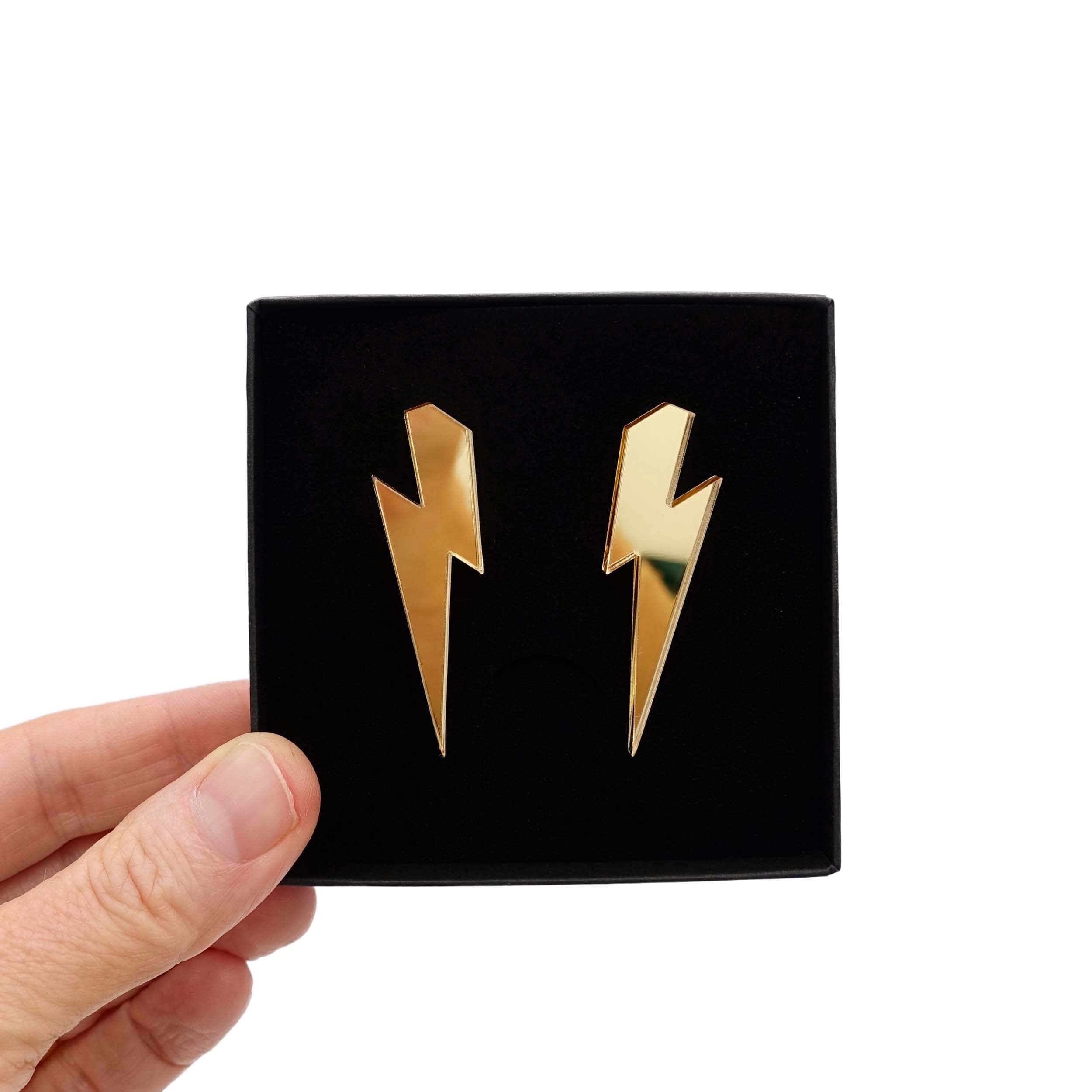 Large Lightning Bolt earrings in gold mirror, shown held up in a Wear and Resist gift box.