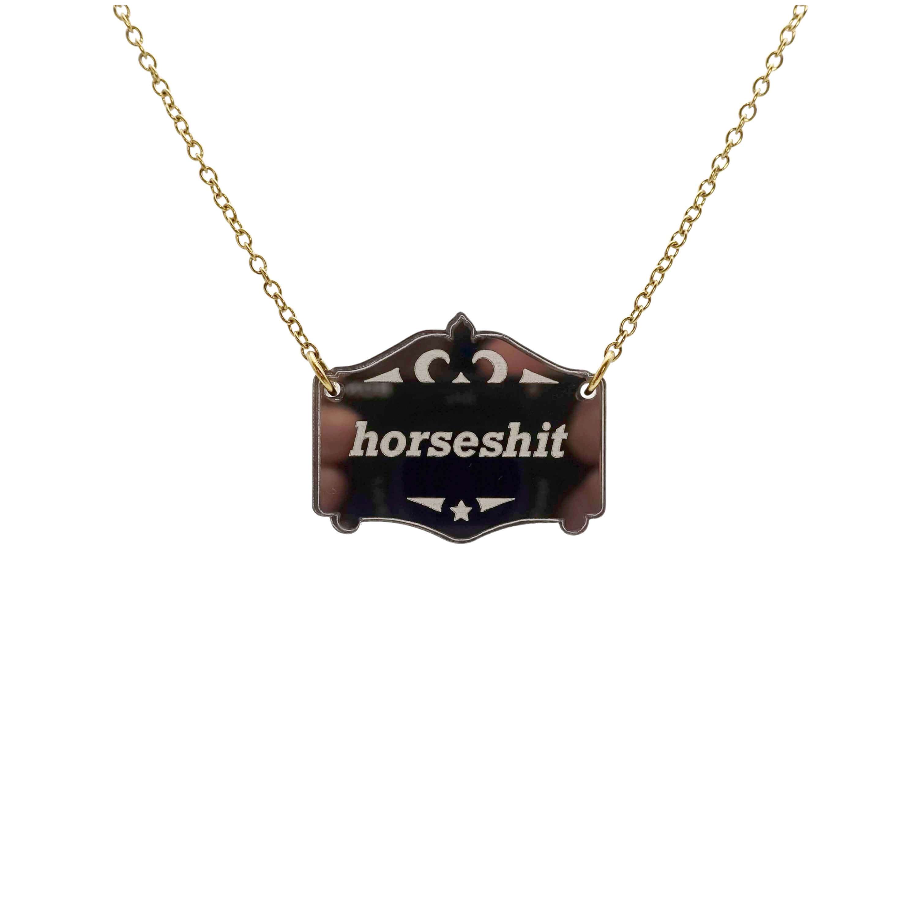 A bronze Mirror Cowboy Horsesh*t necklace, shown hanging on a gold-plated stainless steel chain.