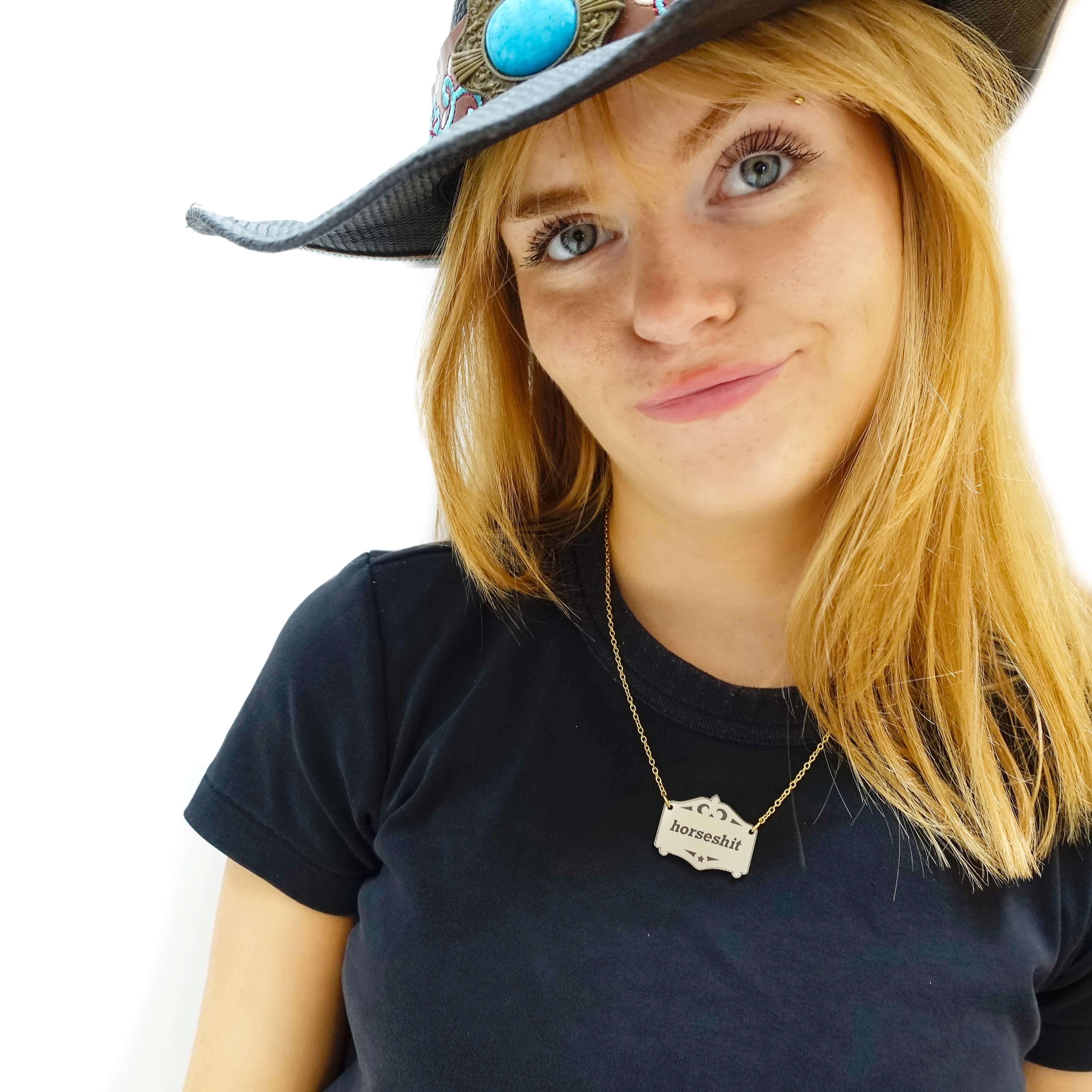 Eliza looks suss wearing a bronze Mirror Cowboy Horsesh*t necklace, on a gold-plated stainless steel chain.