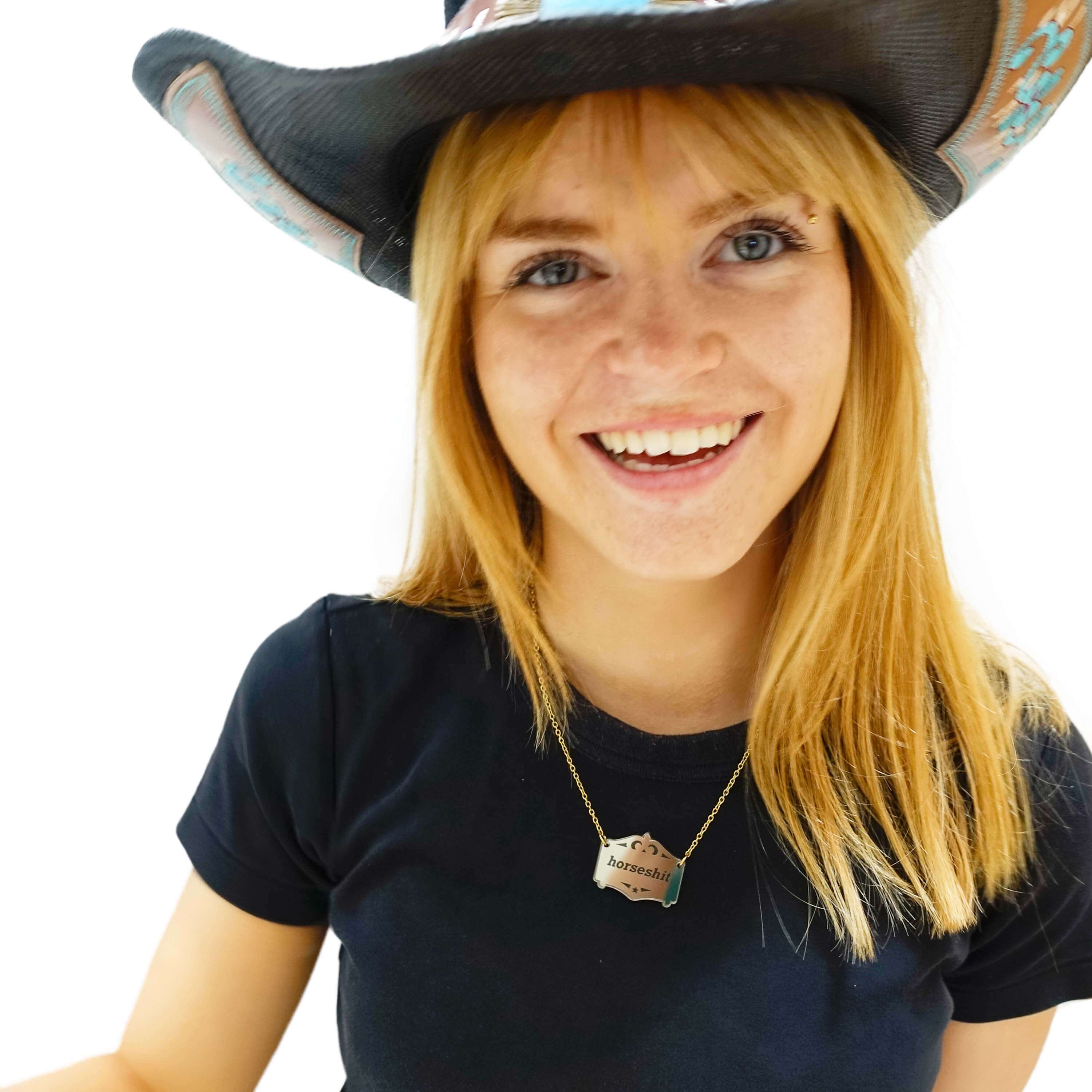 Eliza wears a bronze Mirror Cowboy Horsesh*t necklace, on a gold-plated stainless steel chain.
