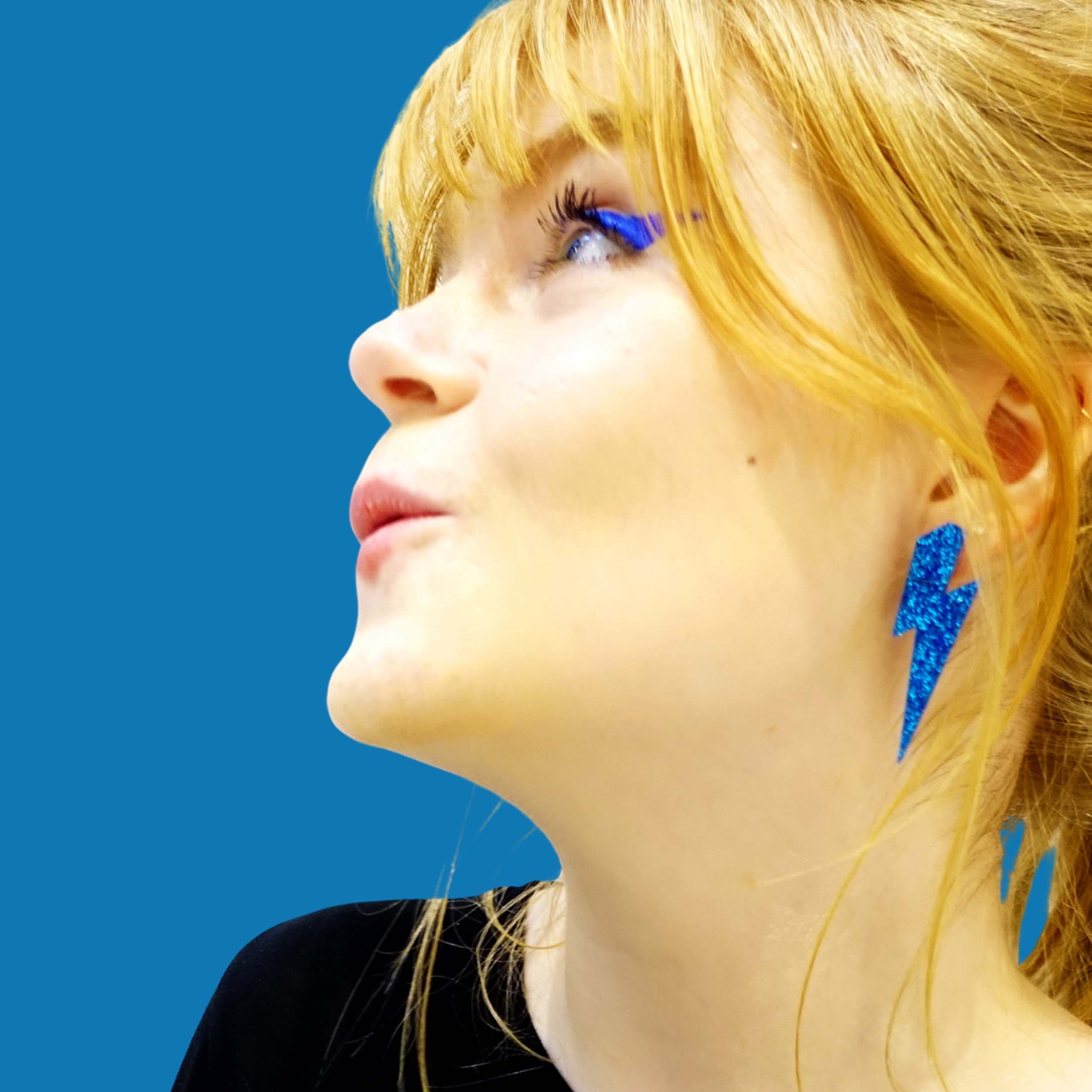Eliza wears large Lightning Bolt earrings in blue glitter.