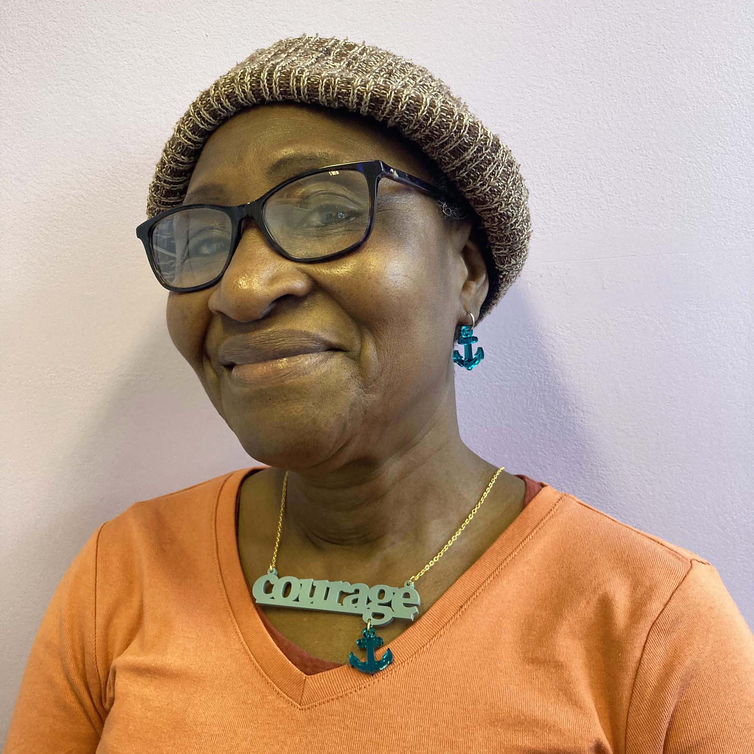 A member of Women for Refugee Women wears medium teal Courage and Hold Fast ancor earrings and a duck egg green Courage necklace from The Courage Collection.