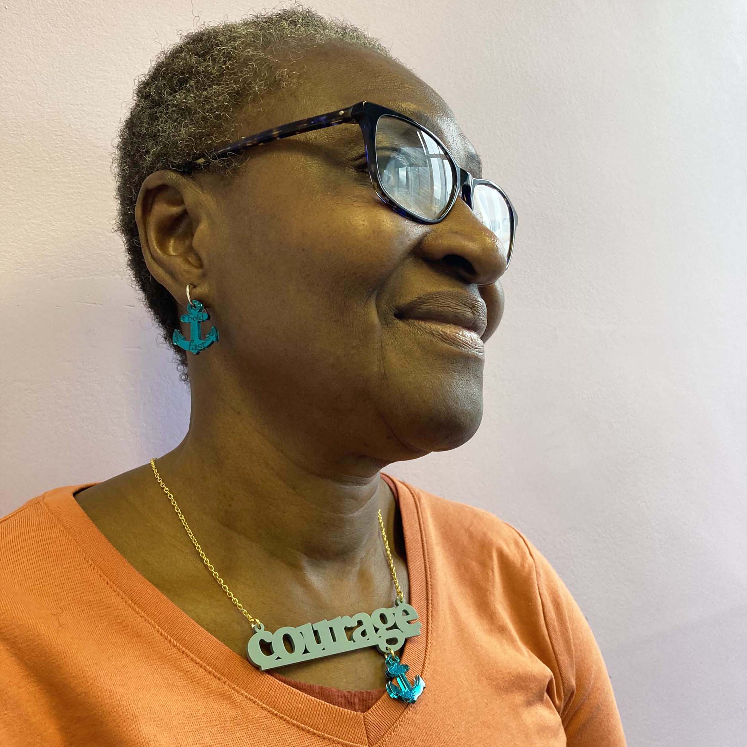 A member of Women for Refugee Women wears medium teal Courage and Hold Fast ancor earrings and a duck egg green Courage necklace from The Courage Collection. £2 from everything in this collection goes to this incredible charity.