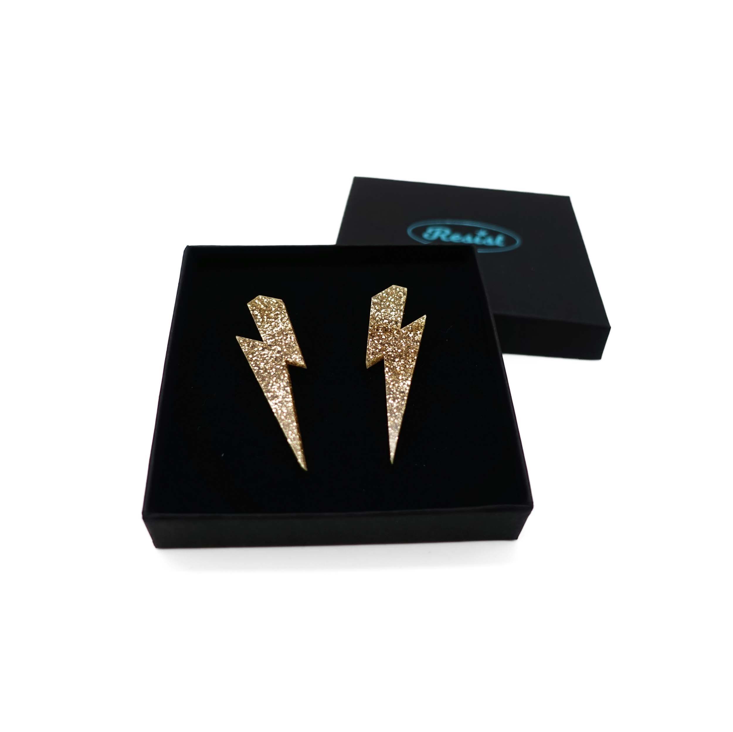 Large Lightning Bolt earrings in gold glitter, shown in a Wear and Resist gift box.