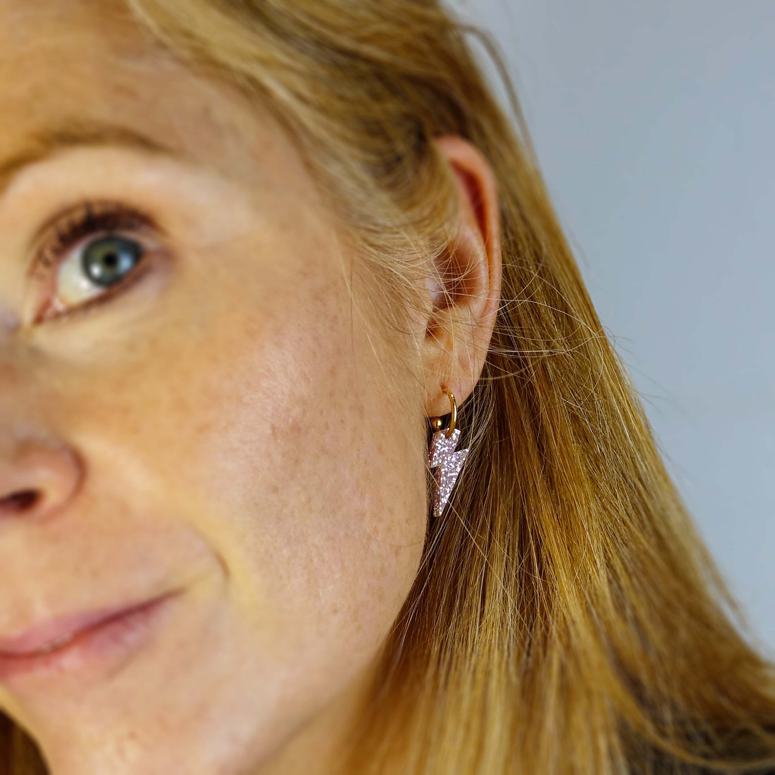 Sarah Day wears Lightning Bolt hoop earrings in pink fizz glitter on gold hoops.