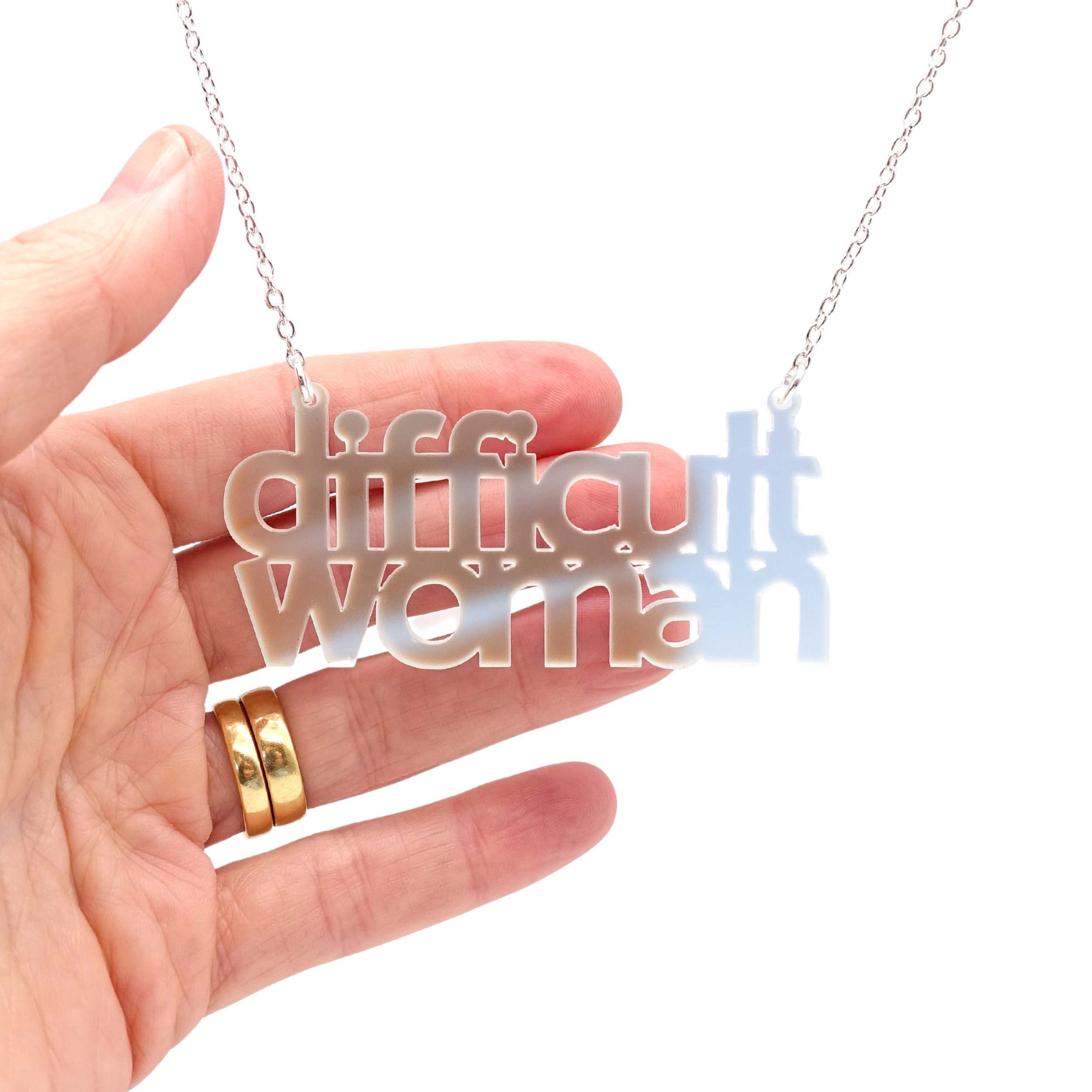 Difficult Woman necklace in matte iridescent, shown hanging against a white background with my hand behind to show the luminosity of the material.