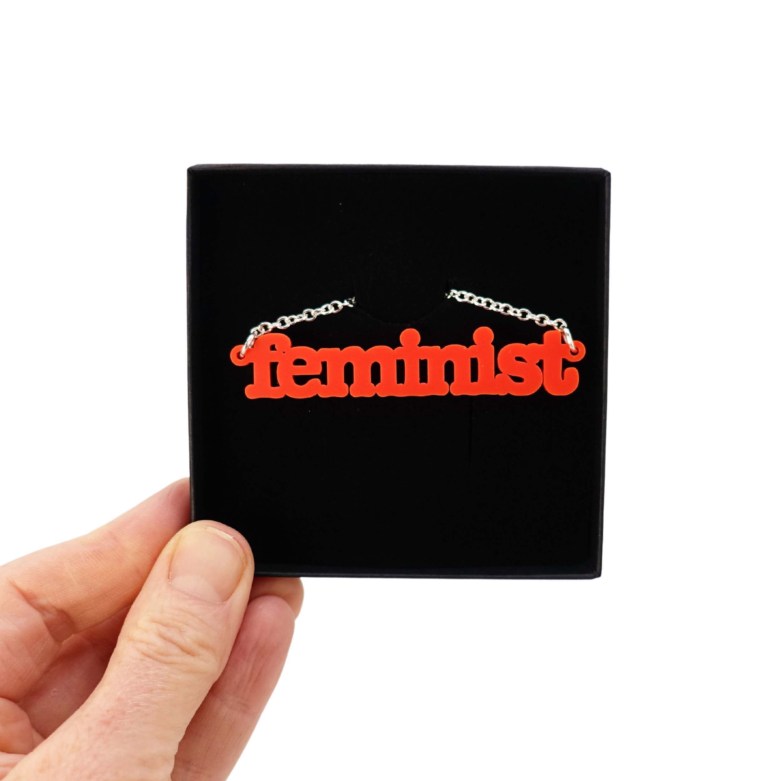 Matte red Feminist necklace shown held up in a Wear and Resist gift box.