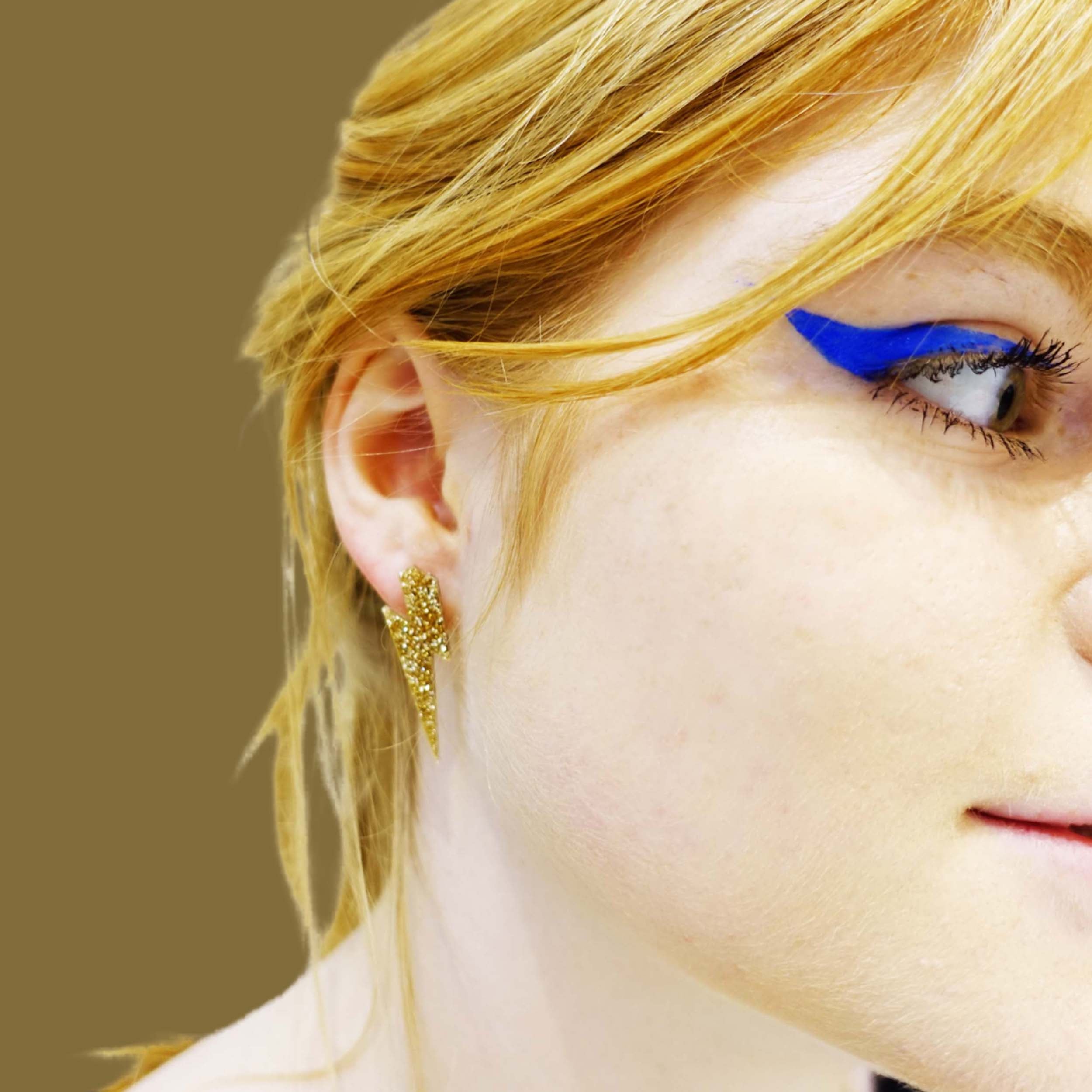 Eliza wears medium Lightning bolt earrings in gold glitter.