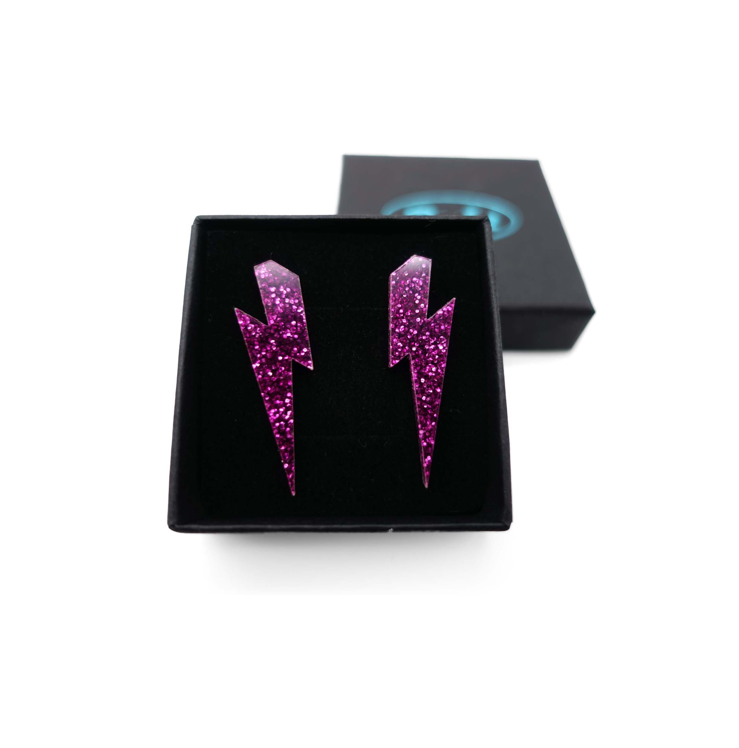 Medium Lightning bolt earrings in purple glitter, shown in a Wear and Resist gift box.
