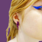 Eliza wears medium Lightning bolt earrings in purple glitter.
