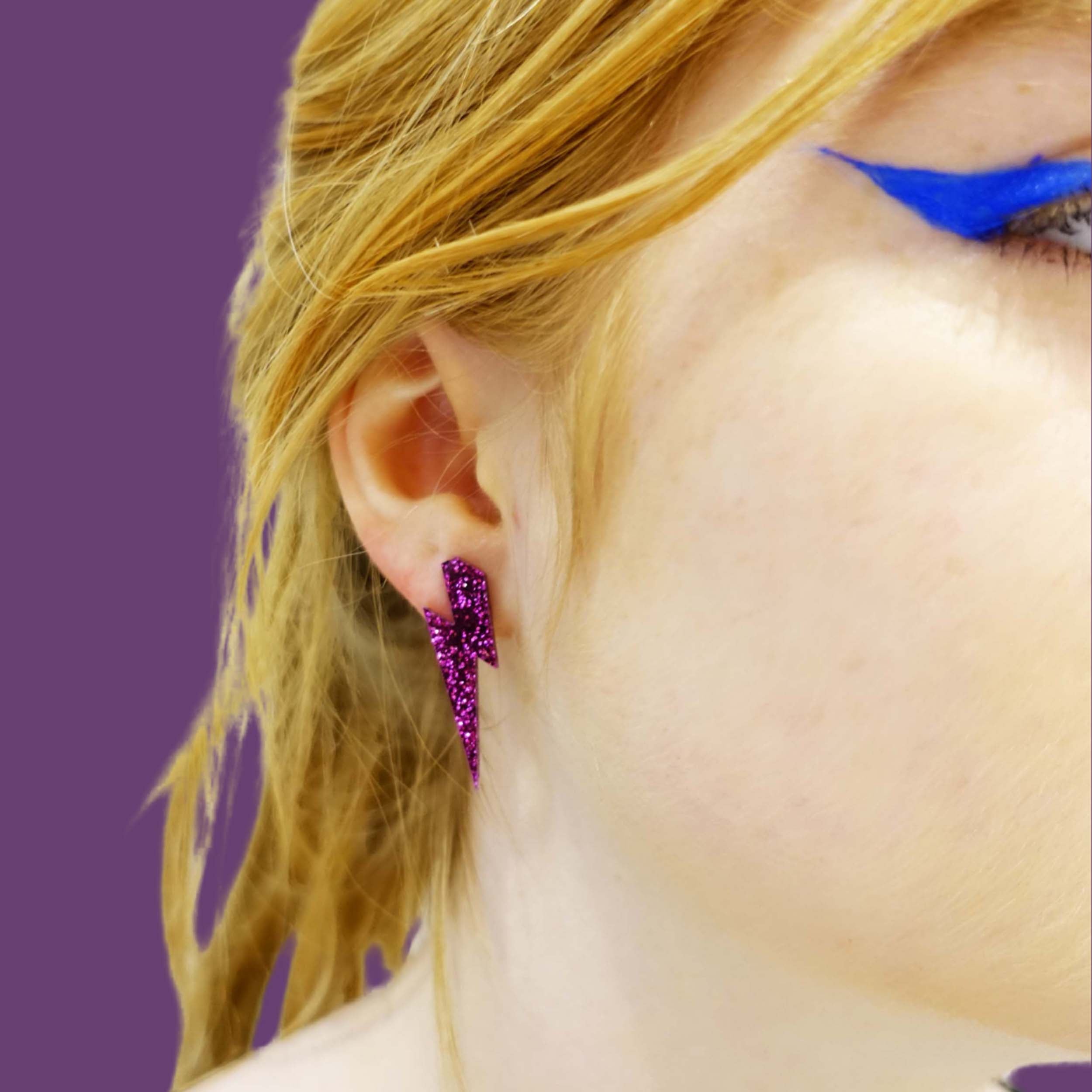 Eliza wears medium Lightning bolt earrings in purple glitter.