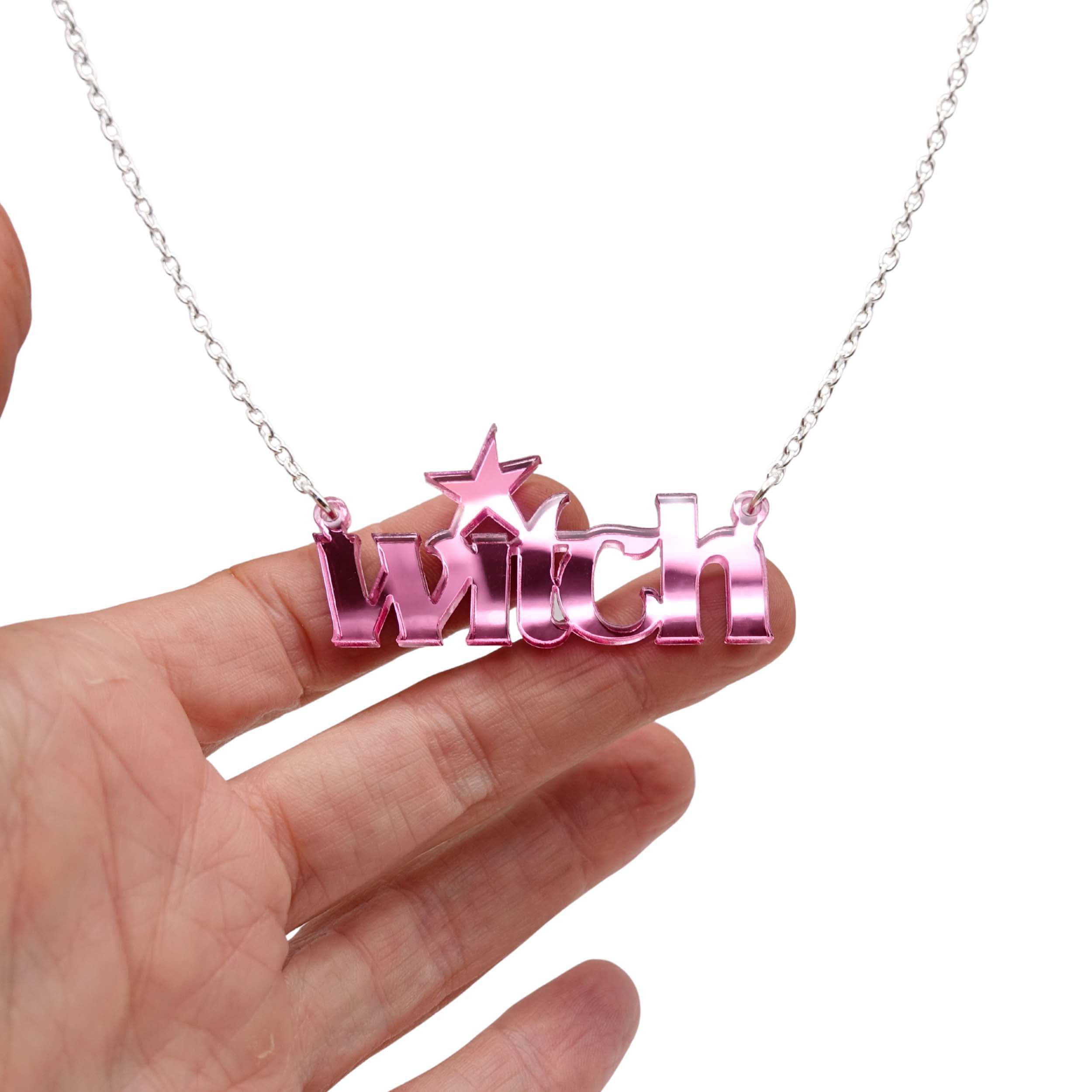 Witch necklace in pink mirror shown hanging against a white background with my hand for size.