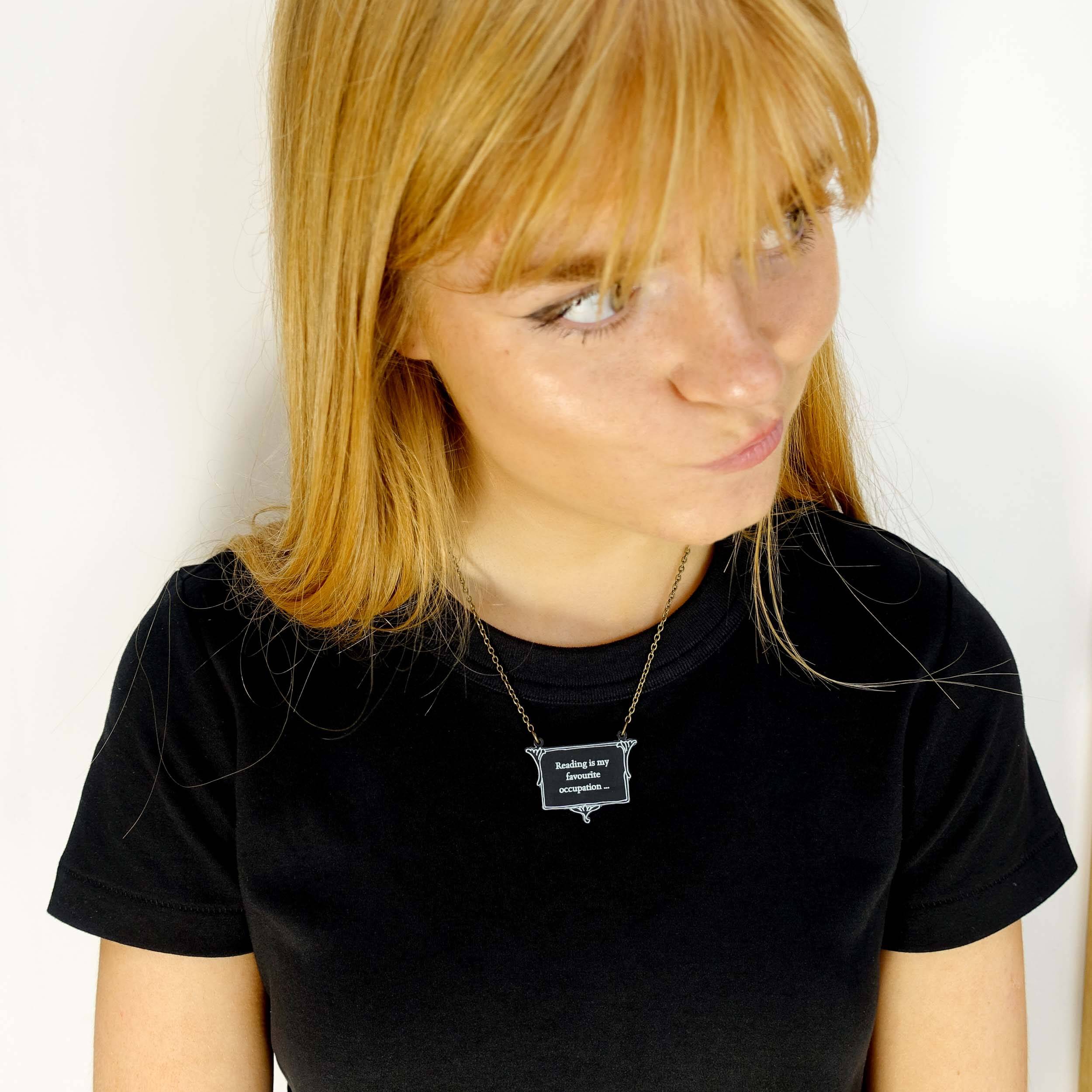 Eliza wears a vintage style slate frost necklace etched with glow-in-the-dark pigment that says, 'Reading is my favourite occupation ...' a quote from Anne Brontë's Agnes Grey.