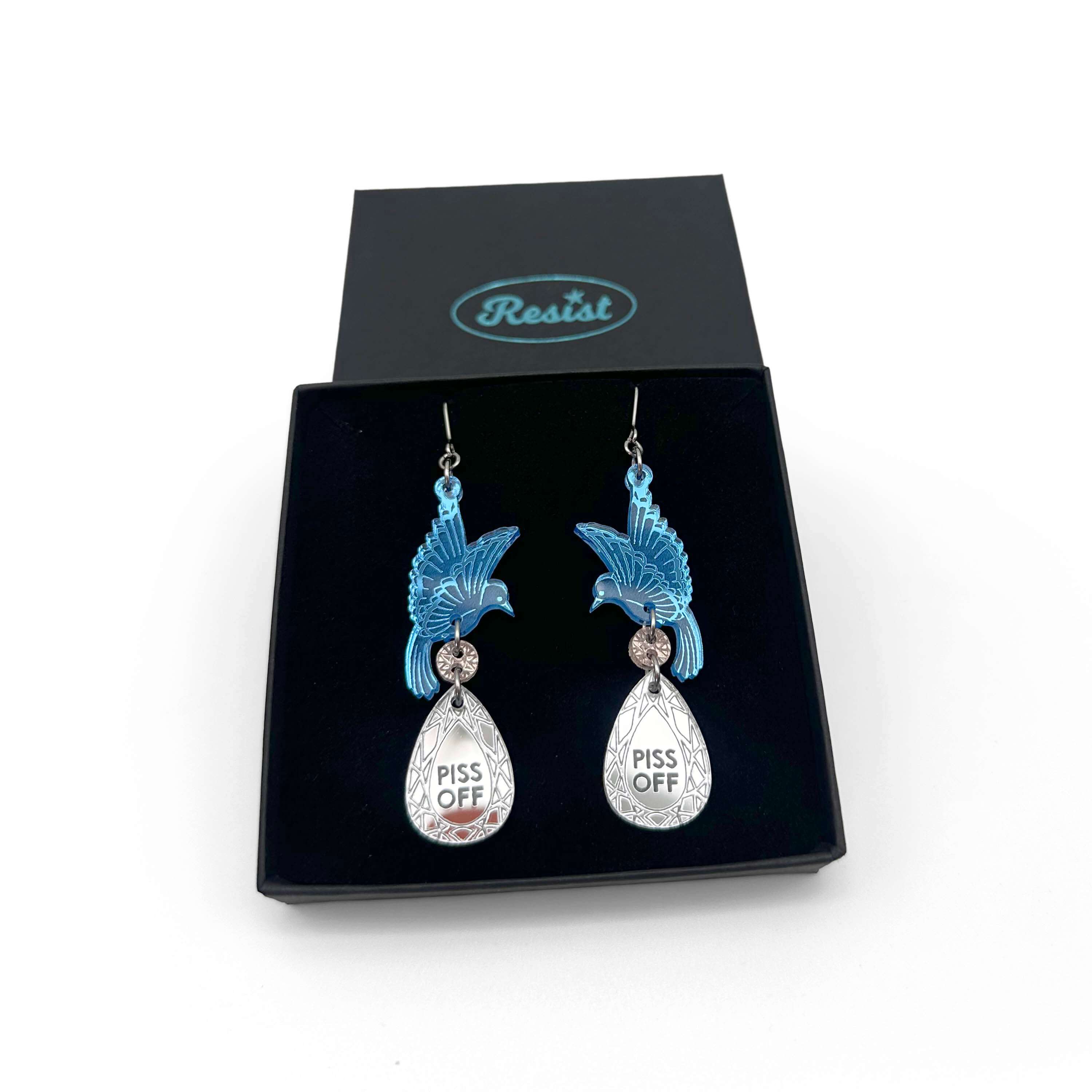 A pair of acrylic earrings with blue birds holding silver 'jewels' that say 'P*ss Off'. Shown in a Wear & Resist gift box.