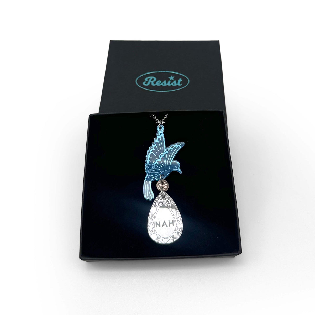 An acrylic pendant necklace with a blue bird holding a silver 'jewel' that says 'Nah.' Shown in a Wear & Resist gift box.
