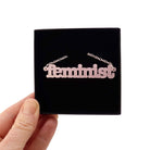 Shell pink Feminist necklace shown held up in a Wear and Resist gift box.