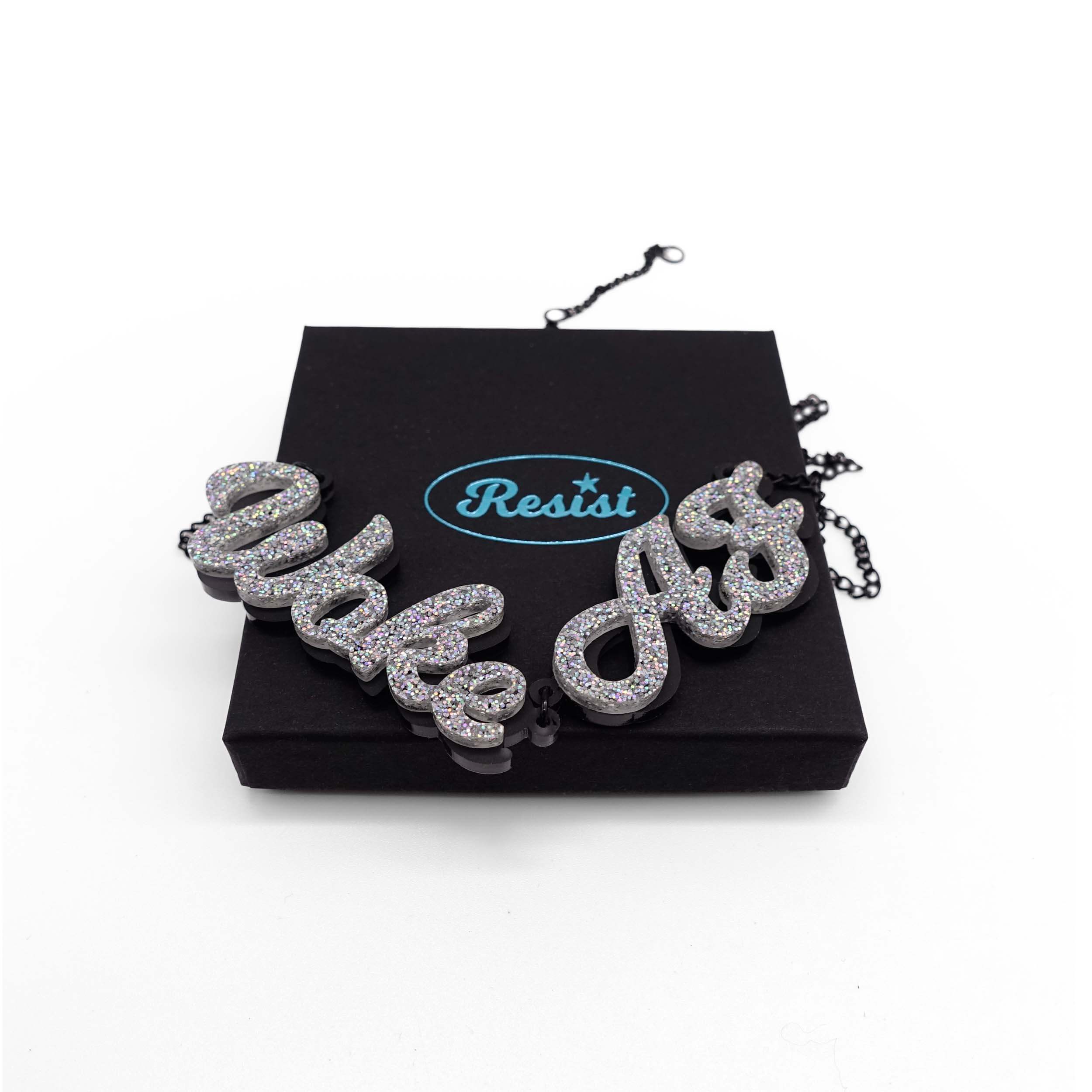 Woke AF necklace in silver glitter shown on a Wear and Resist gift box.