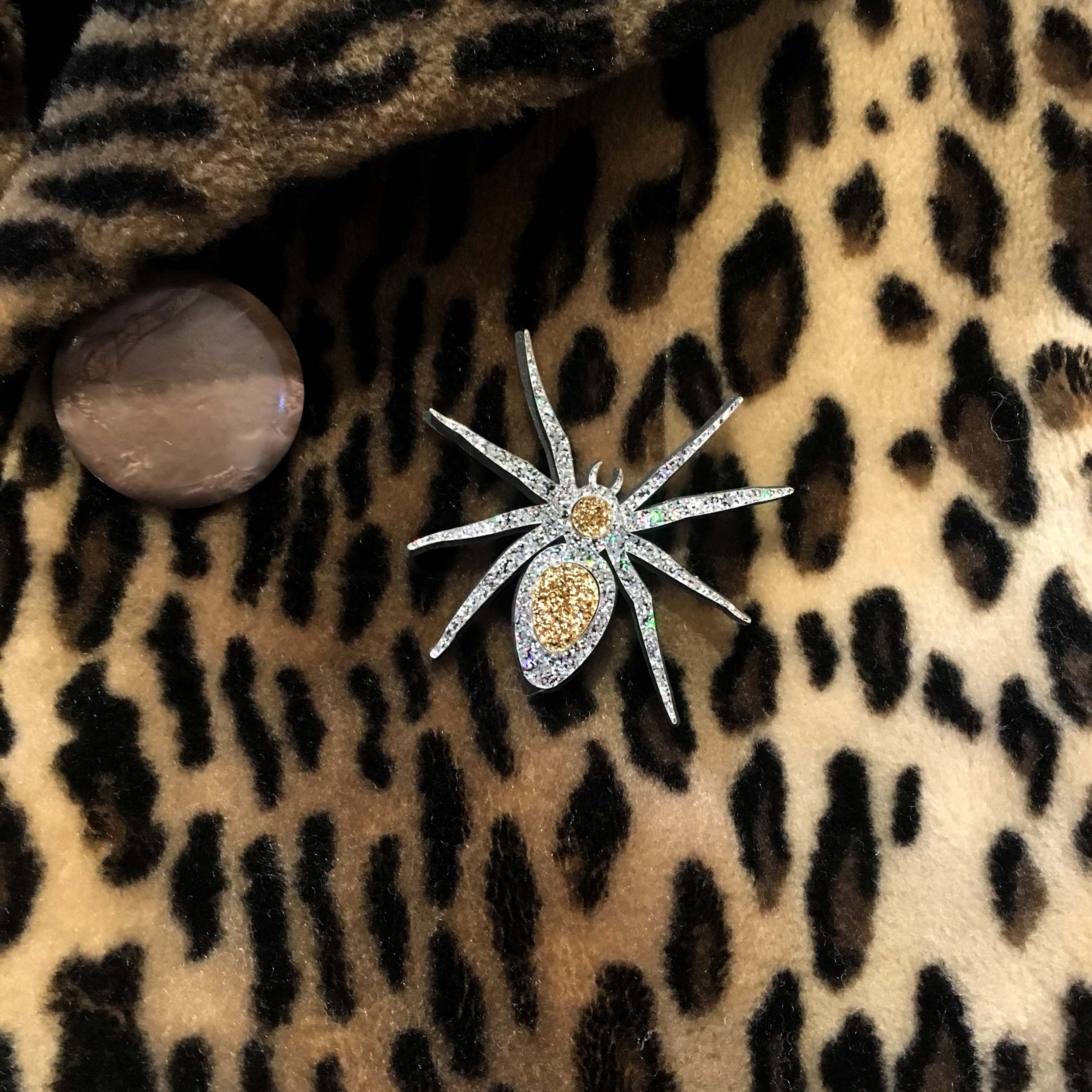 A close up of the All Hail Lady Hail Spider brooch shown on a leopard print coat.
