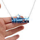 Witch necklace in sky blue mirror  shown hanging against a white background with my hand for size.