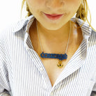 Eliza wears a slate Courage necklace with gold anchor etched with 'hold fast'. It is part of the Courage Collection designed by Wear and Resist supporting Women for Refugee Women.