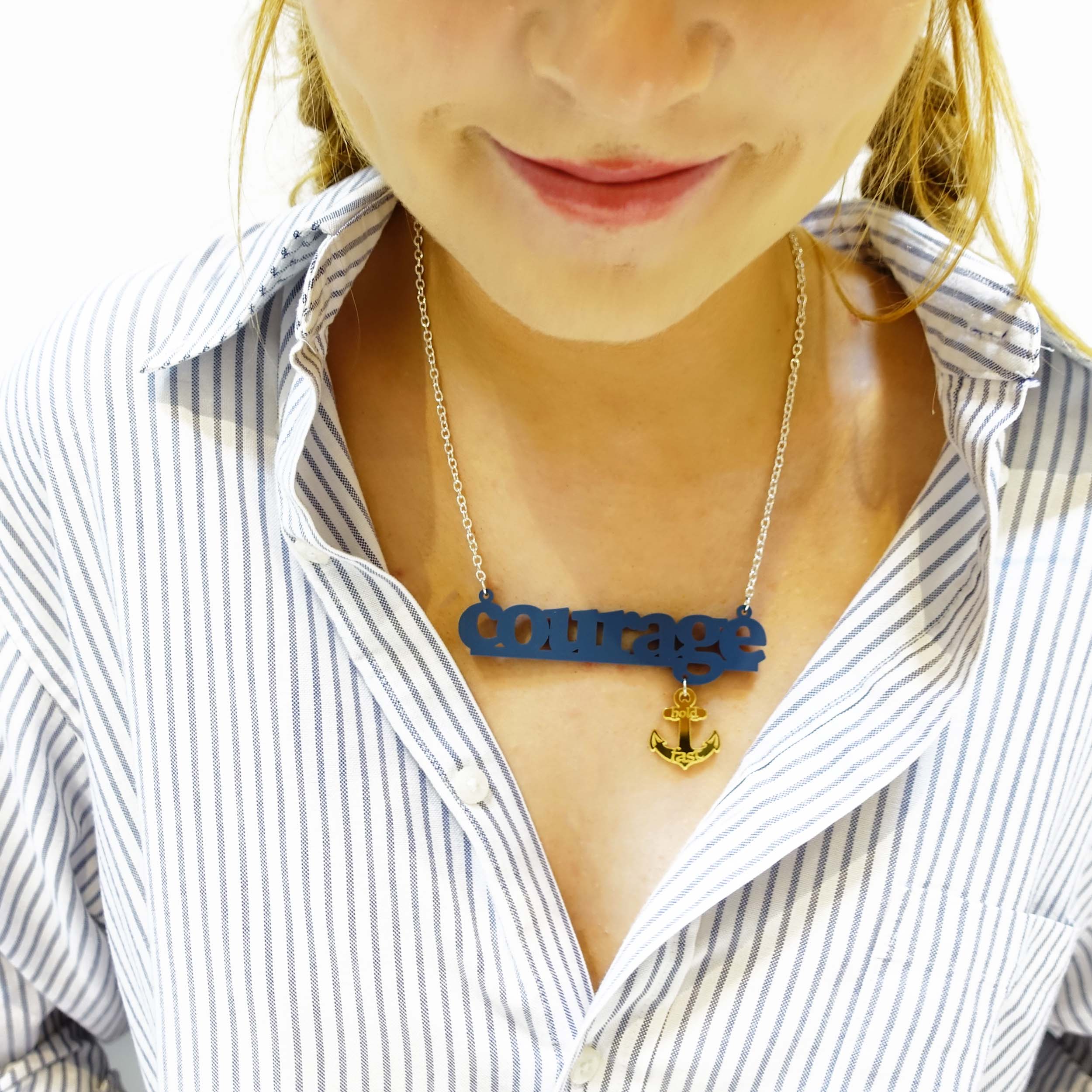 Eliza wears a slate Courage necklace with gold anchor etched with 'hold fast'. It is part of the Courage Collection designed by Wear and Resist supporting Women for Refugee Women.