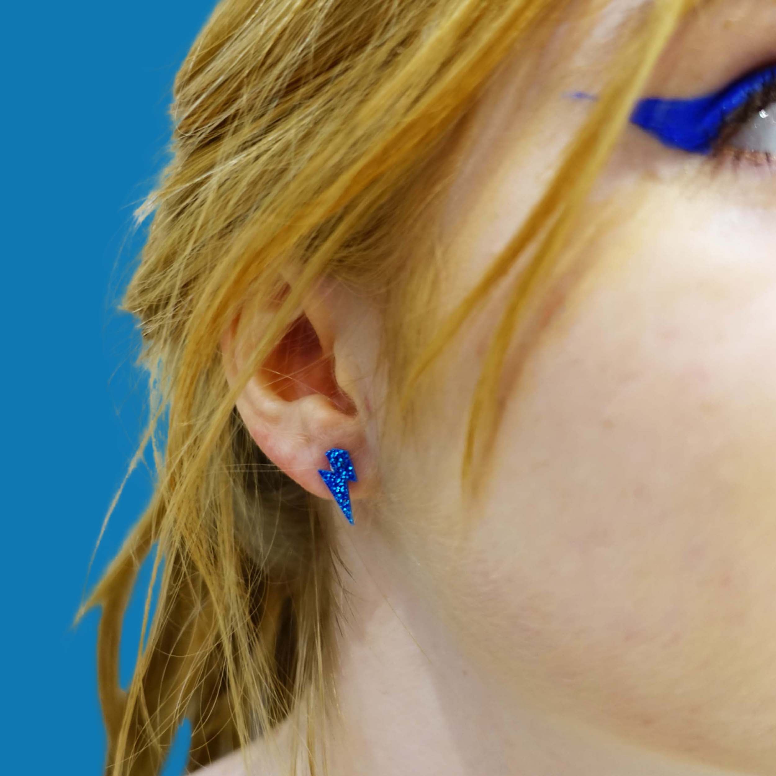 Eliza wears tiny Lightning bolt earrings in blue glitter.