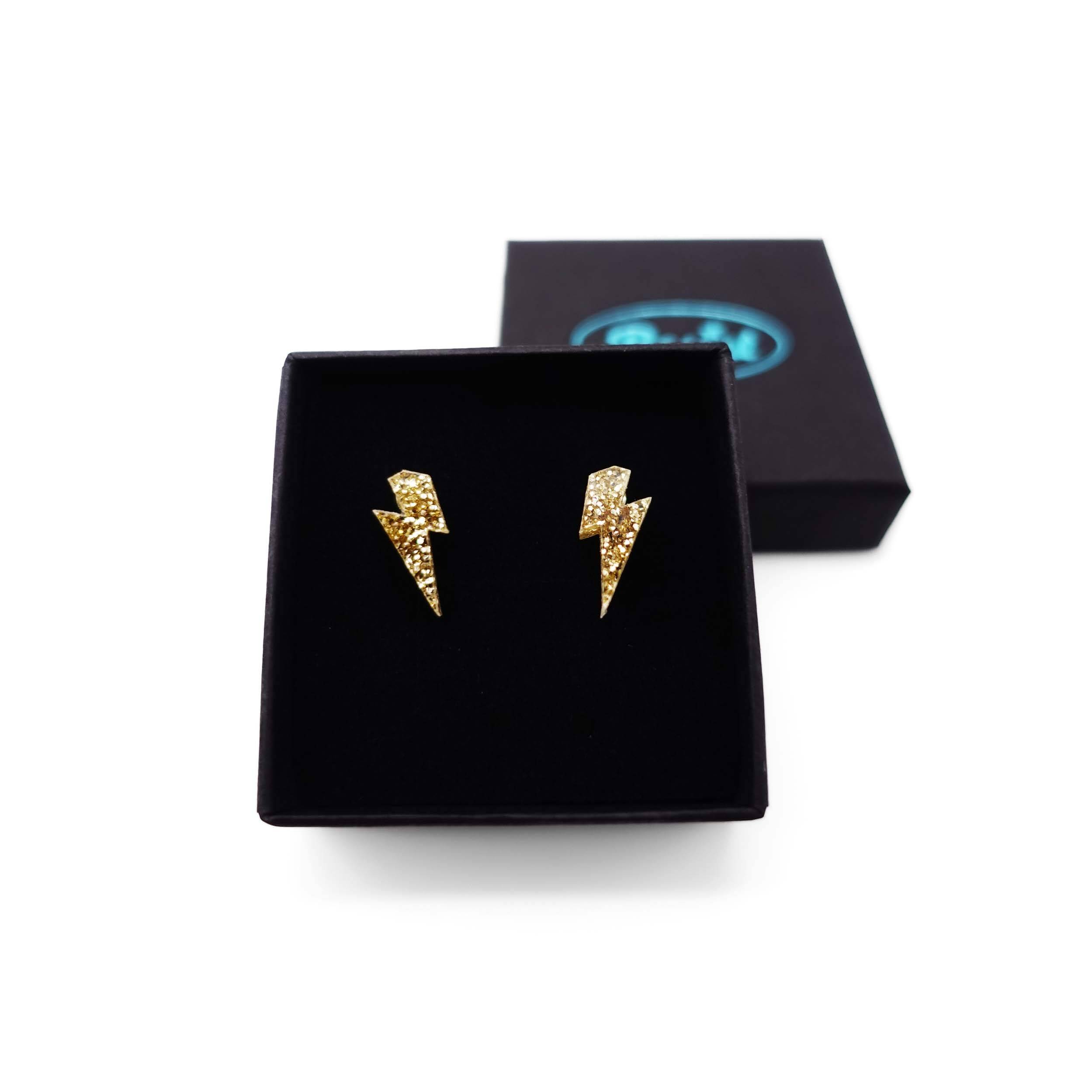 Tiny Lightning Bolt earrings in gold glitter, shown in a Wear and Resist gift box.