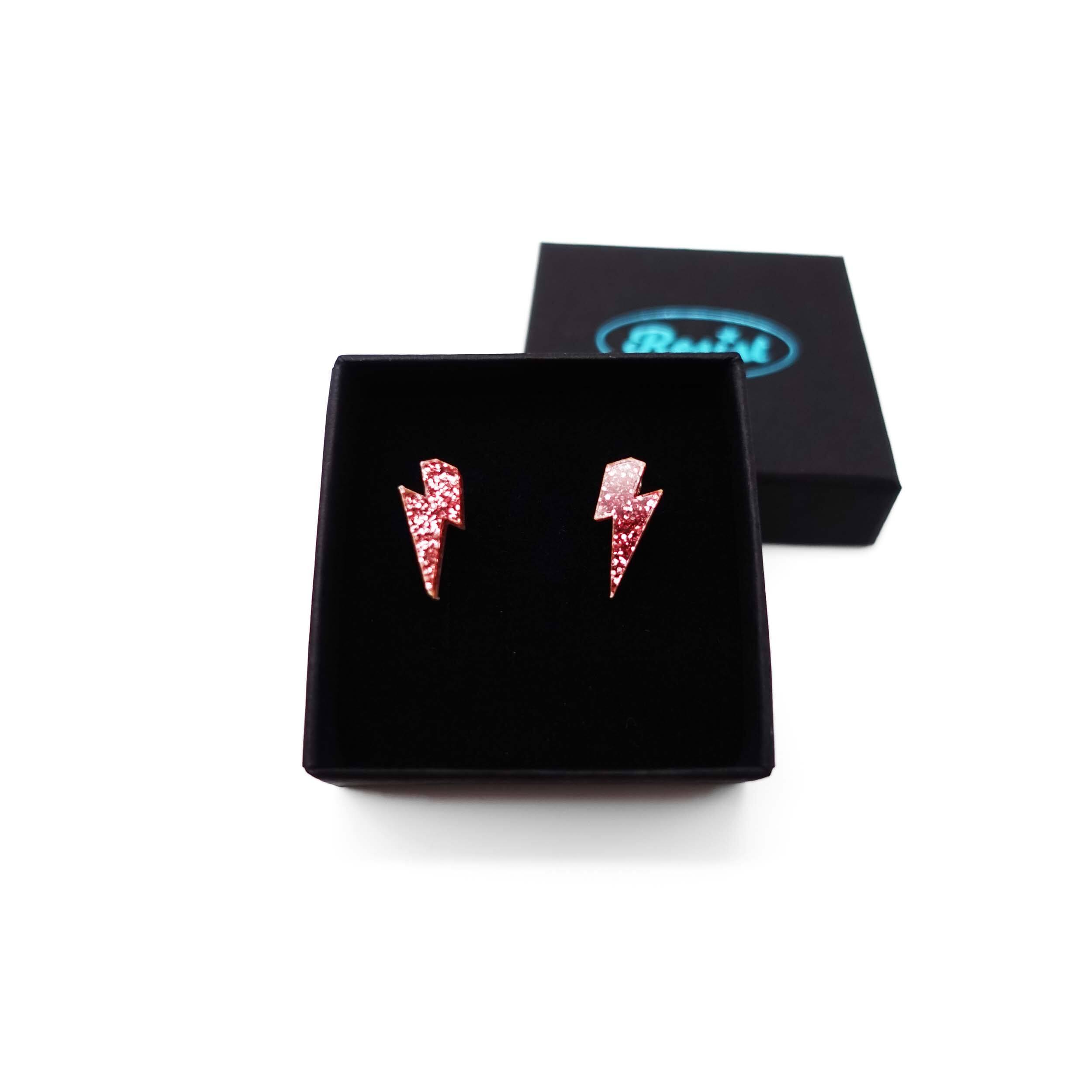 Tiny Lightning Bolt earrings in rose glitter, shown in a Wear and Resist gift box.