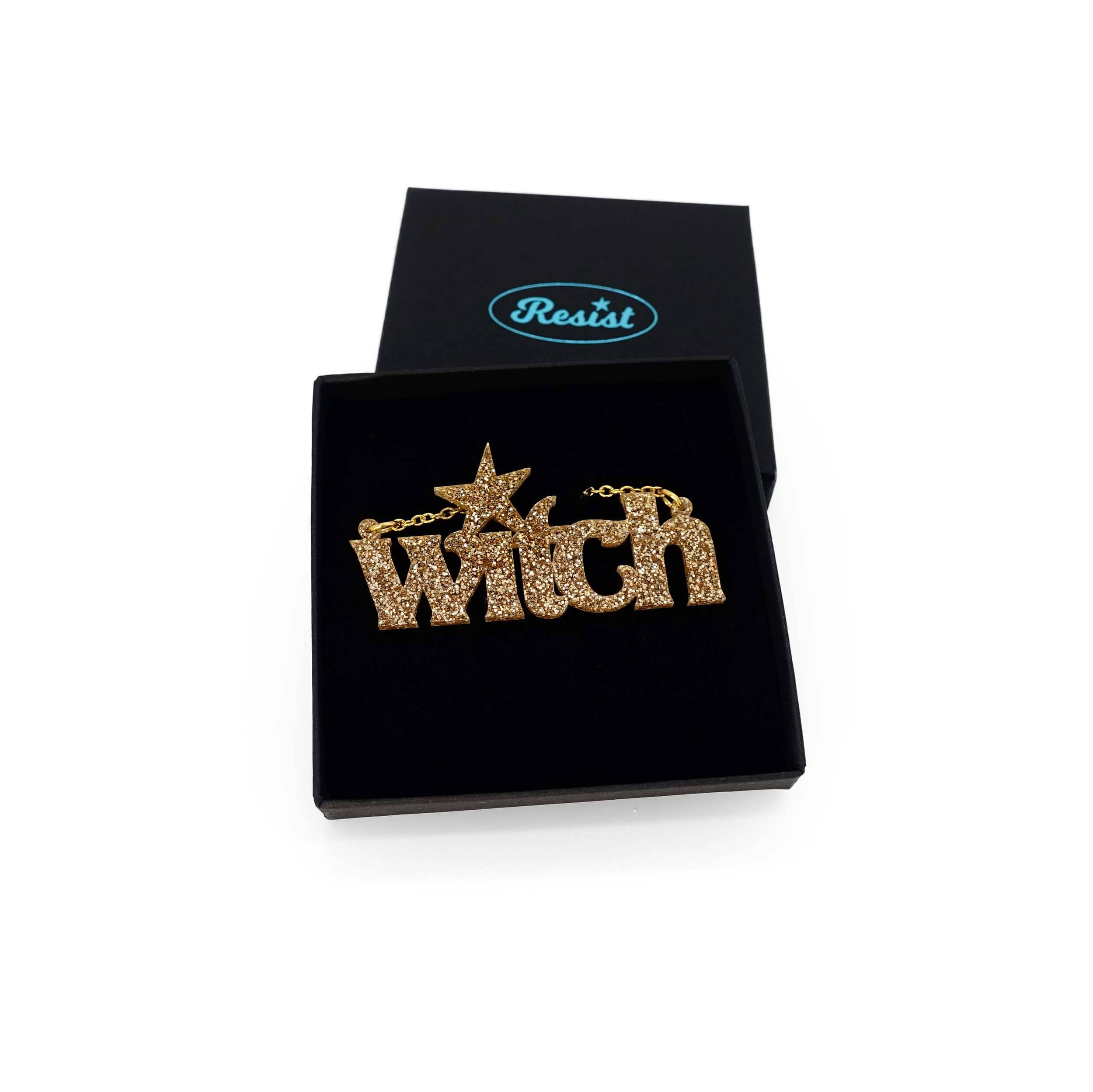 Gold glitter Witch necklace shown in a Wear and Resist gift box.