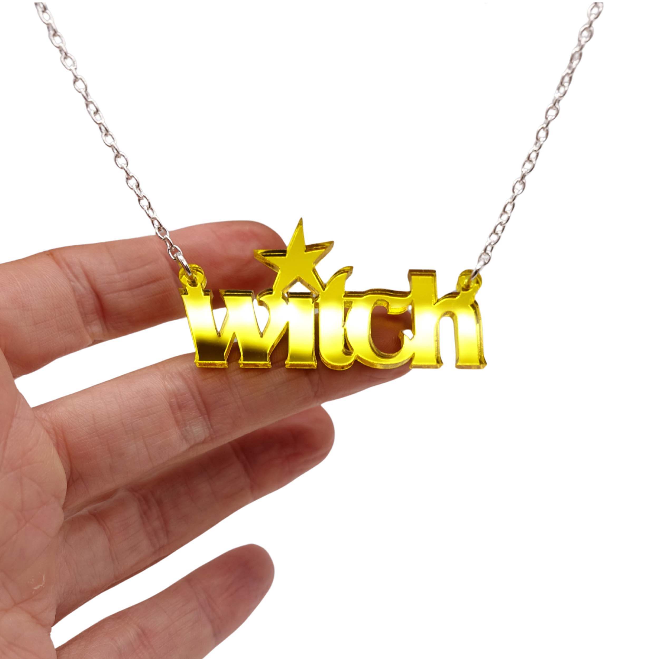 Witch necklace in yellow mirror shown hanging against a white background with my hand for size.