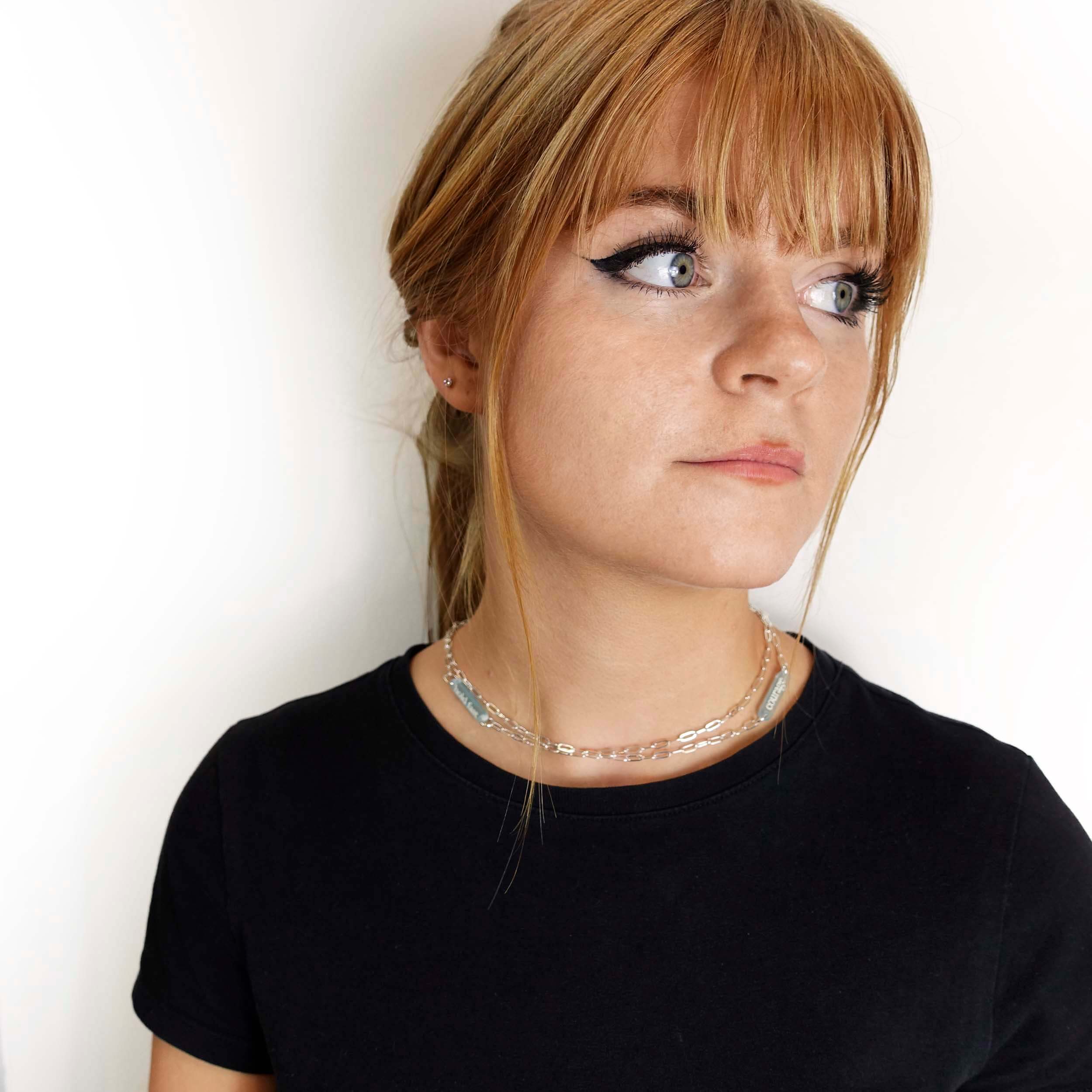 Eliza wears the Have a Word with Yourself design on a silver plated paperclip chain as a shorter necklace, with the words 'courage' and 'hold fast' etched in glow-in-the-dark pigment, finished with a small anchor charm.