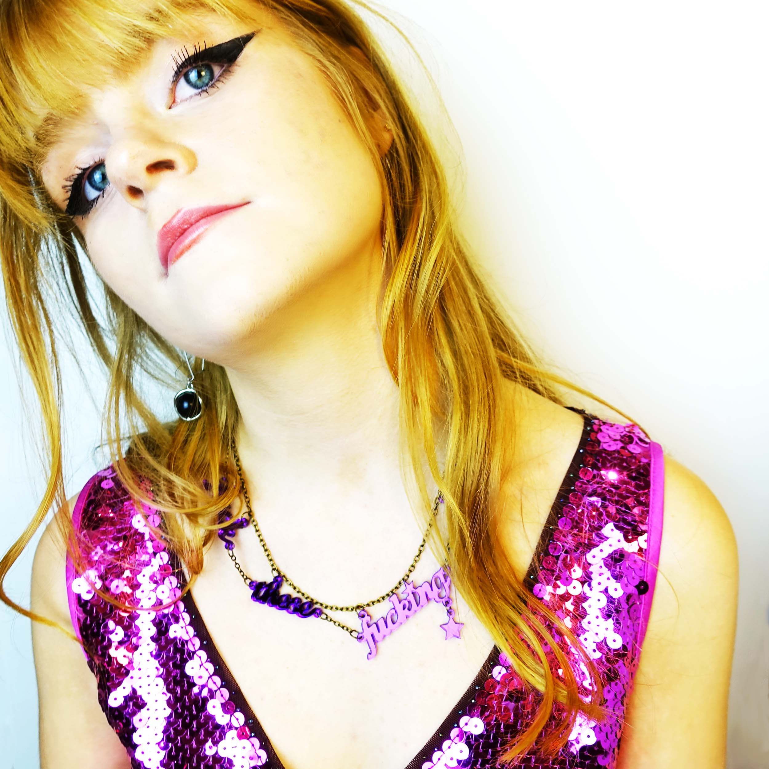 Eliza wears a F*ck these F*cking F*ckers necklace in purple mirror,  by Wear and Resist, and a very pretty pink sequin dress.