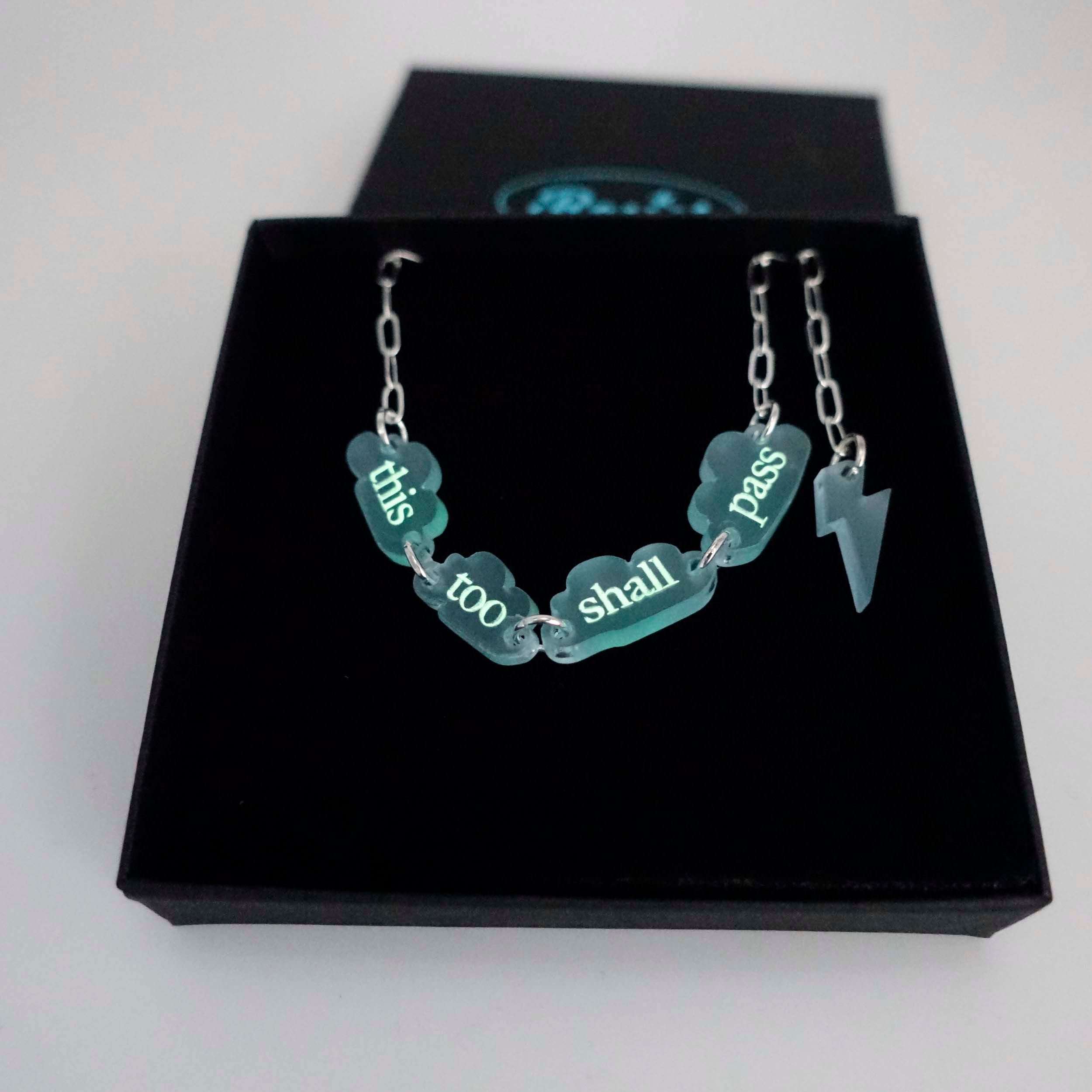 This too shall pass floating clouds necklace on a silver-plated paper-clip chain with lightning bolt charm, shown in a Wear and Resist gift box.