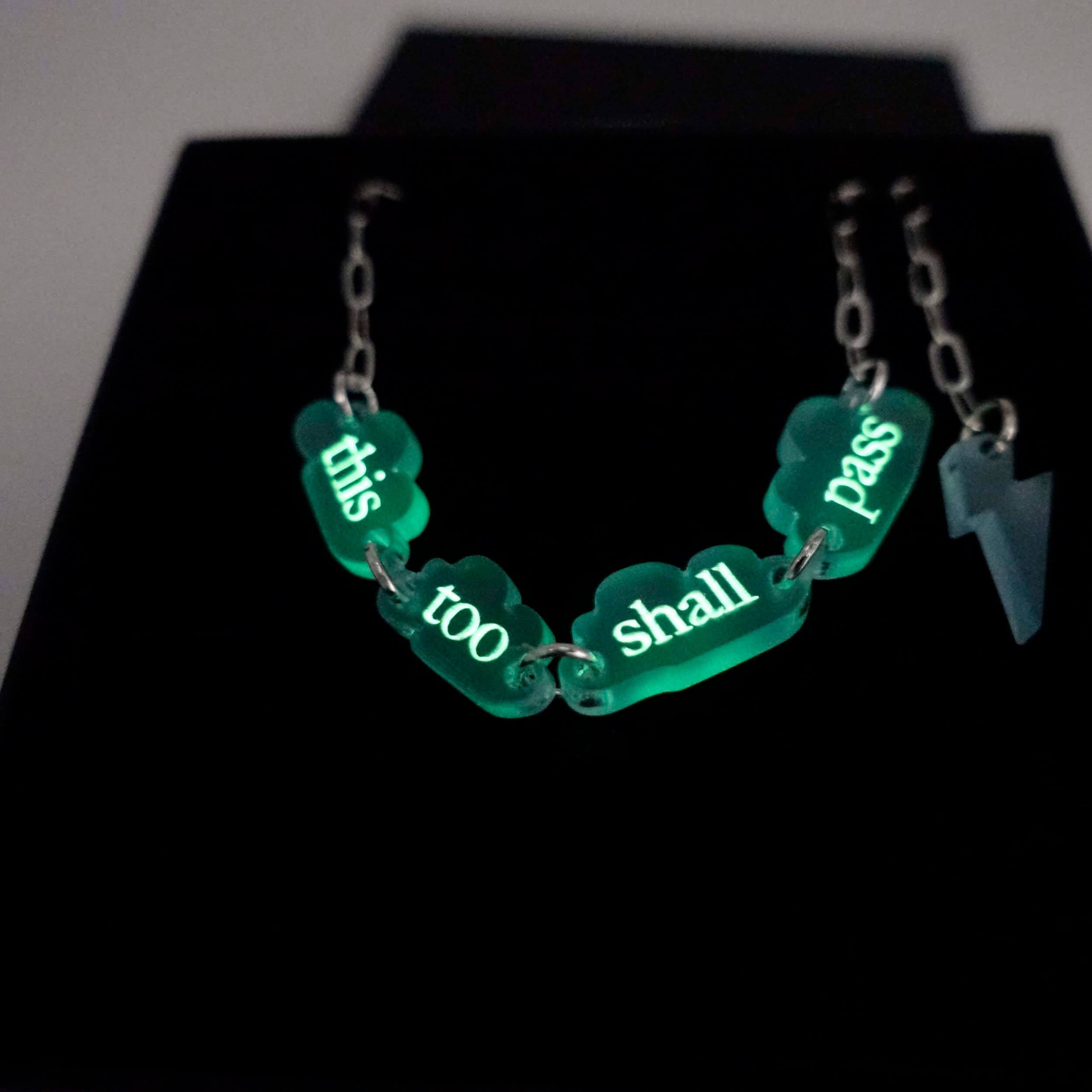 Close up of This too shall pass floating clouds necklace glowing in the half-light.