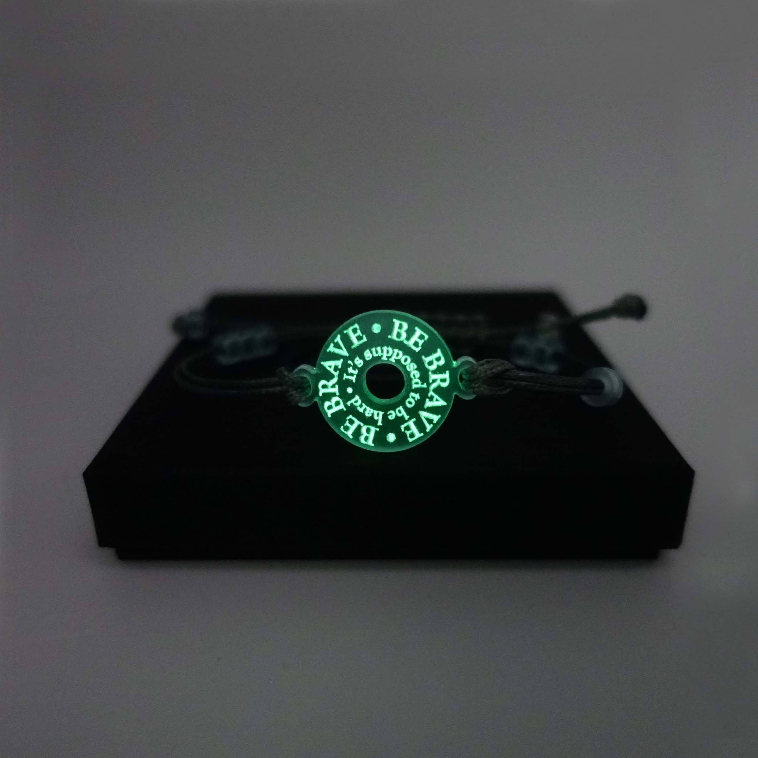 Hand-tied friendship style bracelet inscribed with 'Be brave. It's supposed to be hard,' in glow in the dark pigment. Shown on a Wear and Resist gift box.