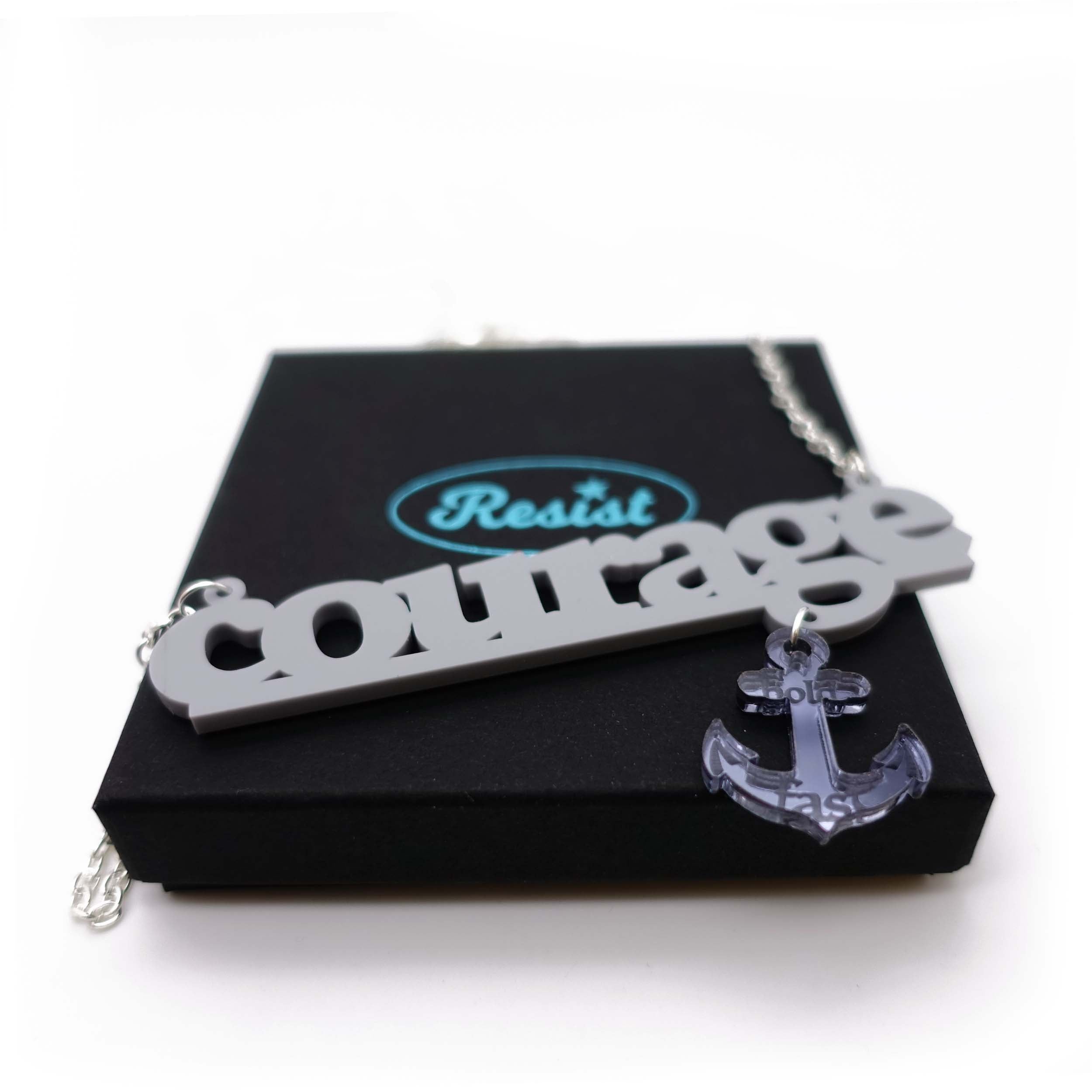 Courage necklace in grey with slate dangling anchor etched with the words, 'hold fast,' shown on a Wear and Resist gift box.