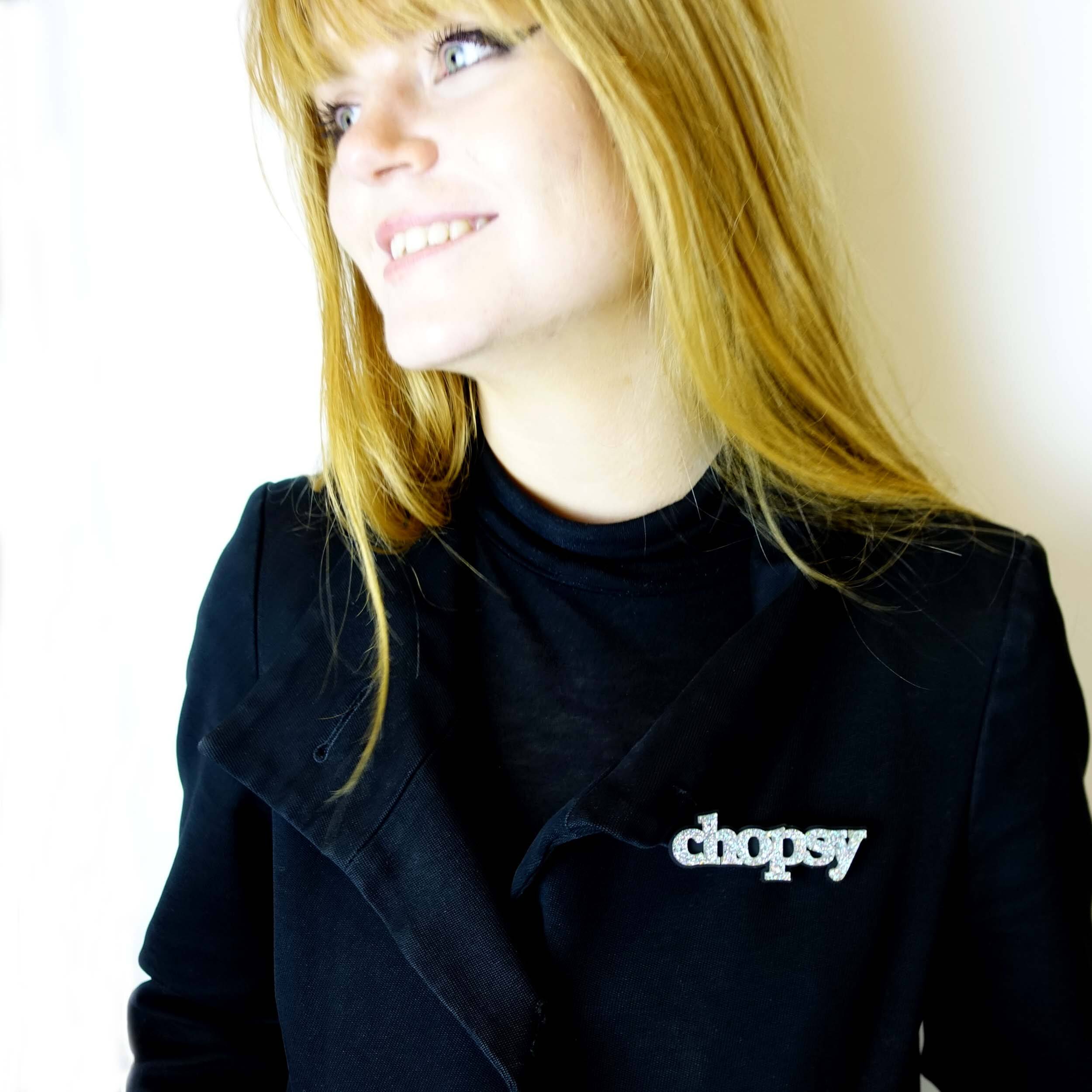 Model wears and iridescent silver glitter Chopsy brooch designed by Sarah Day for Wear and Resist. £2 goes to Welsh Women's Aid. Fel yr arfer, mae £2 o bob mwclus Chopsy yn mynd at @welshwomensaid.