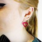 Eliza wears small transparent hot pink love heart hoop earrings.