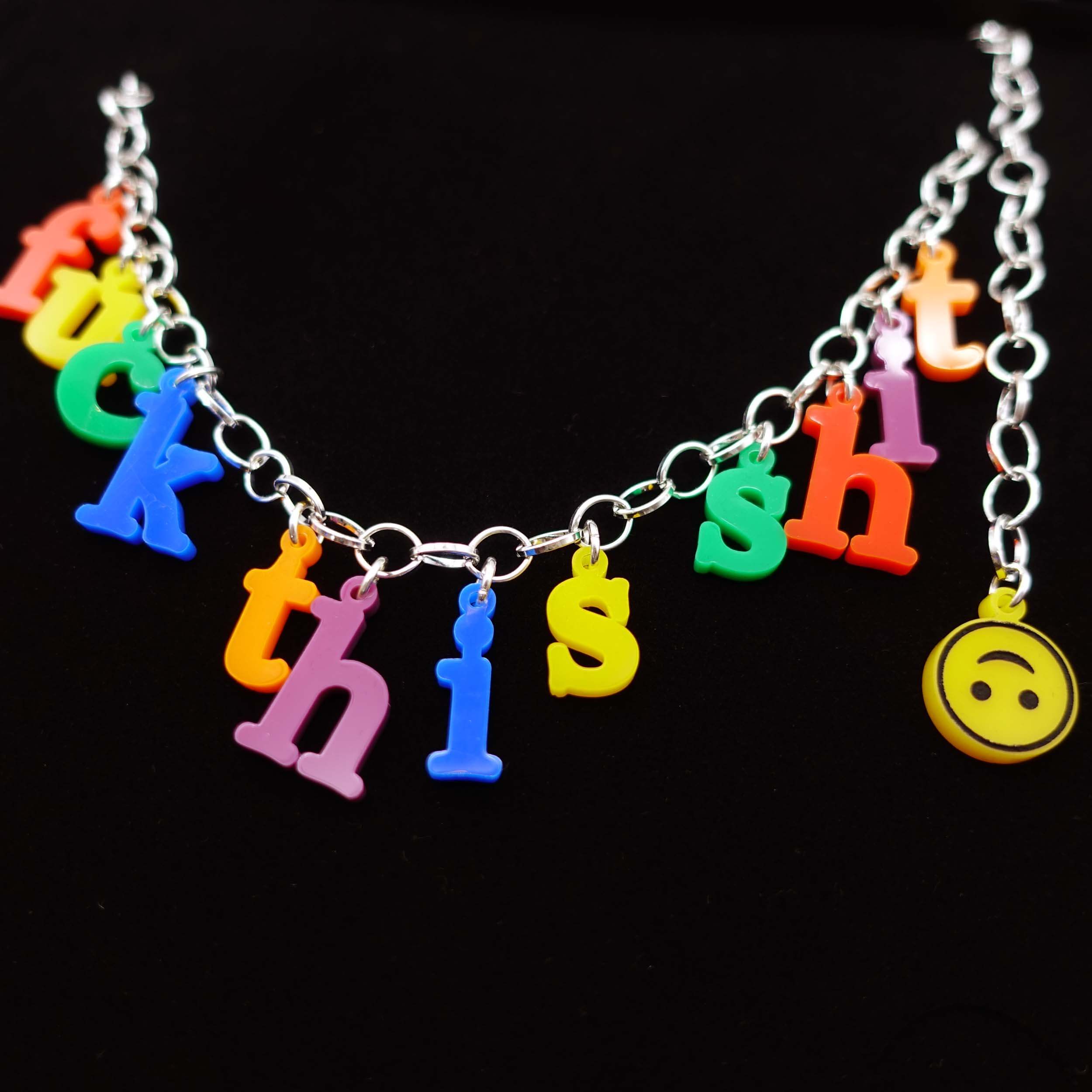 A close up of F*ck this sh*t necklace in retro alphabet fridge magnet style letters with an upside down smiley face to finish the chain.