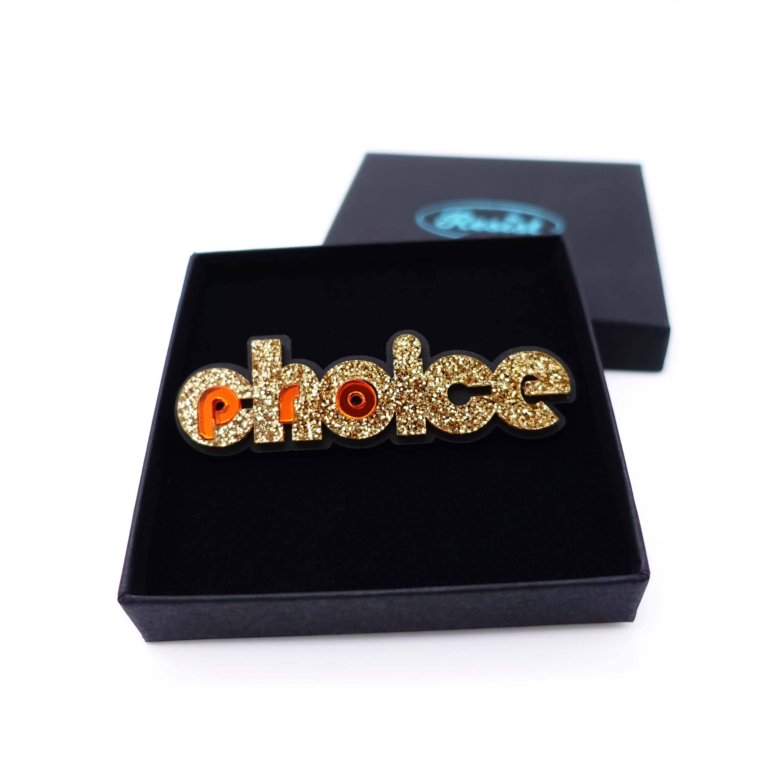 Gold glitter and flame Pro-choice brooch, designed by Sarah Day for Wear and Resist, shown in a gift box.
