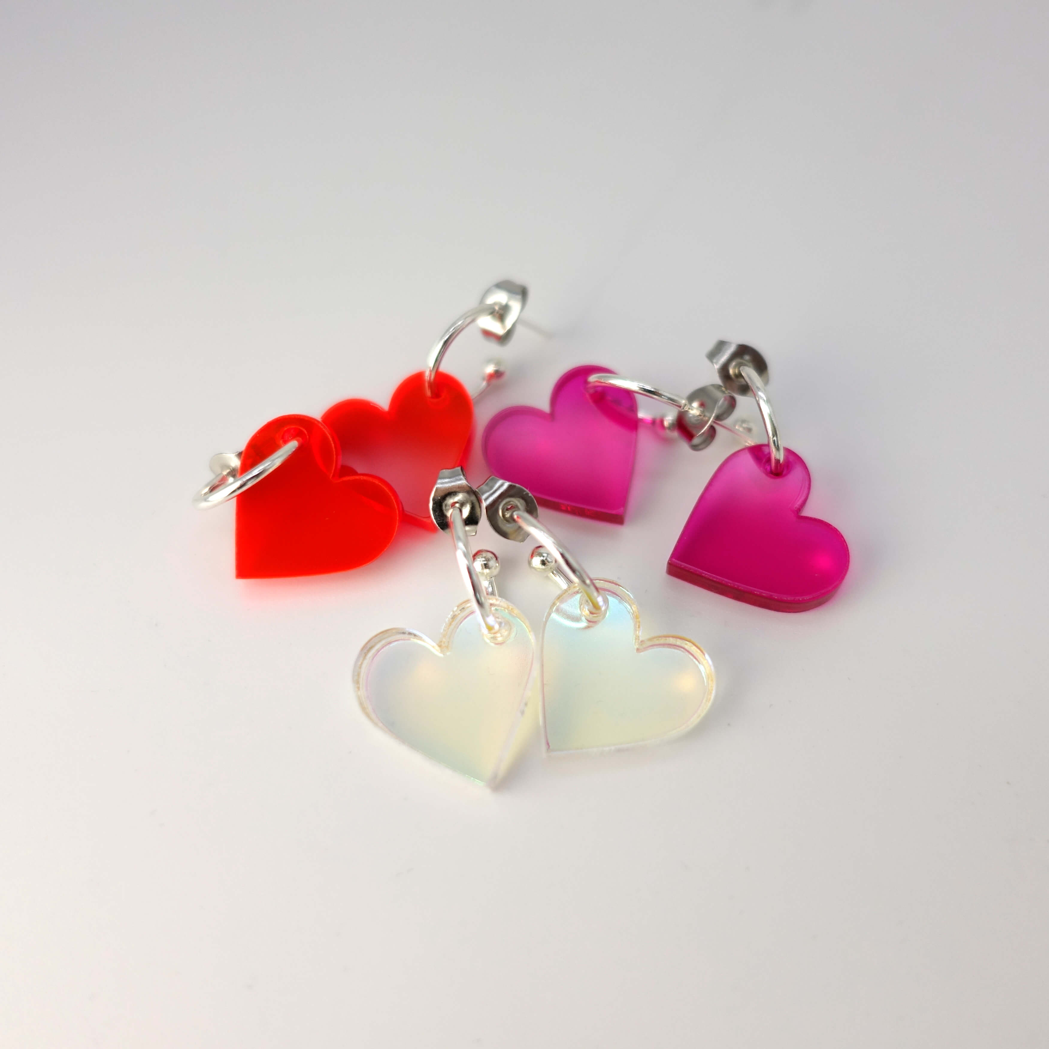 A group shot of all the three colours of simple heart earrings: neon pink, hot red and iridescent on silver-plated hoops.