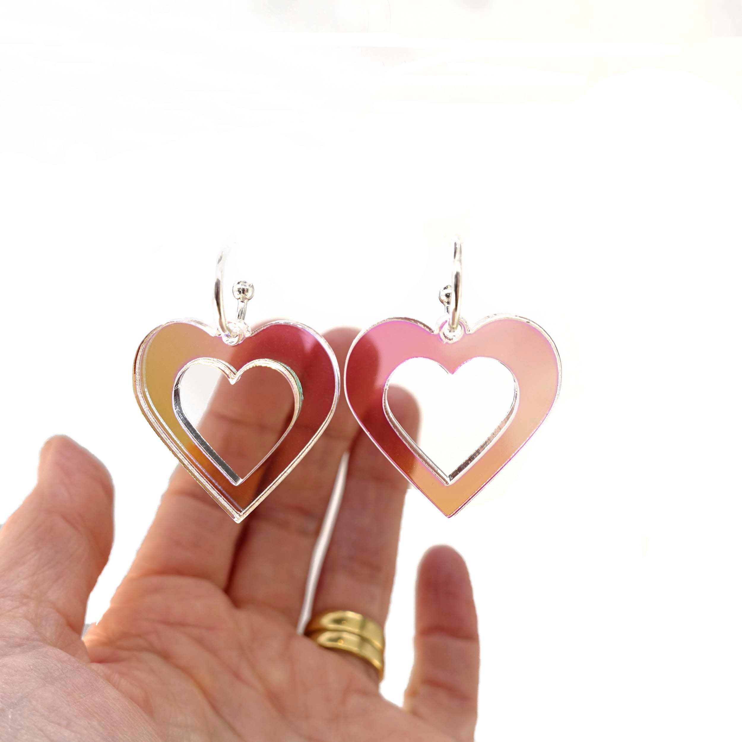 Big heart hoops in iridescent on silver hoops, shown against a white background with my hand behind to show scale and the transparency of the material.
