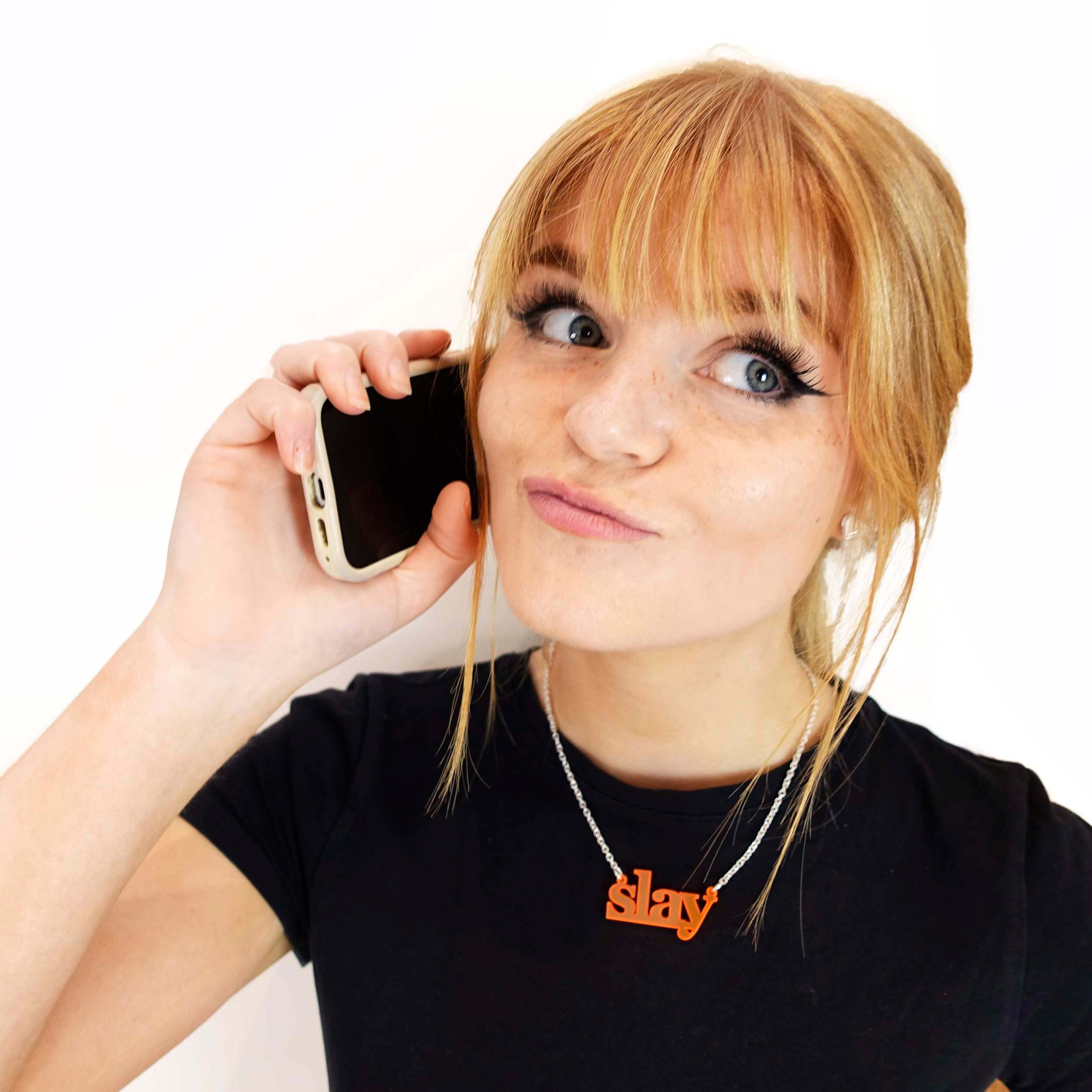 Eliza wears a fluoro orange Slay necklace as she slays on the phone.