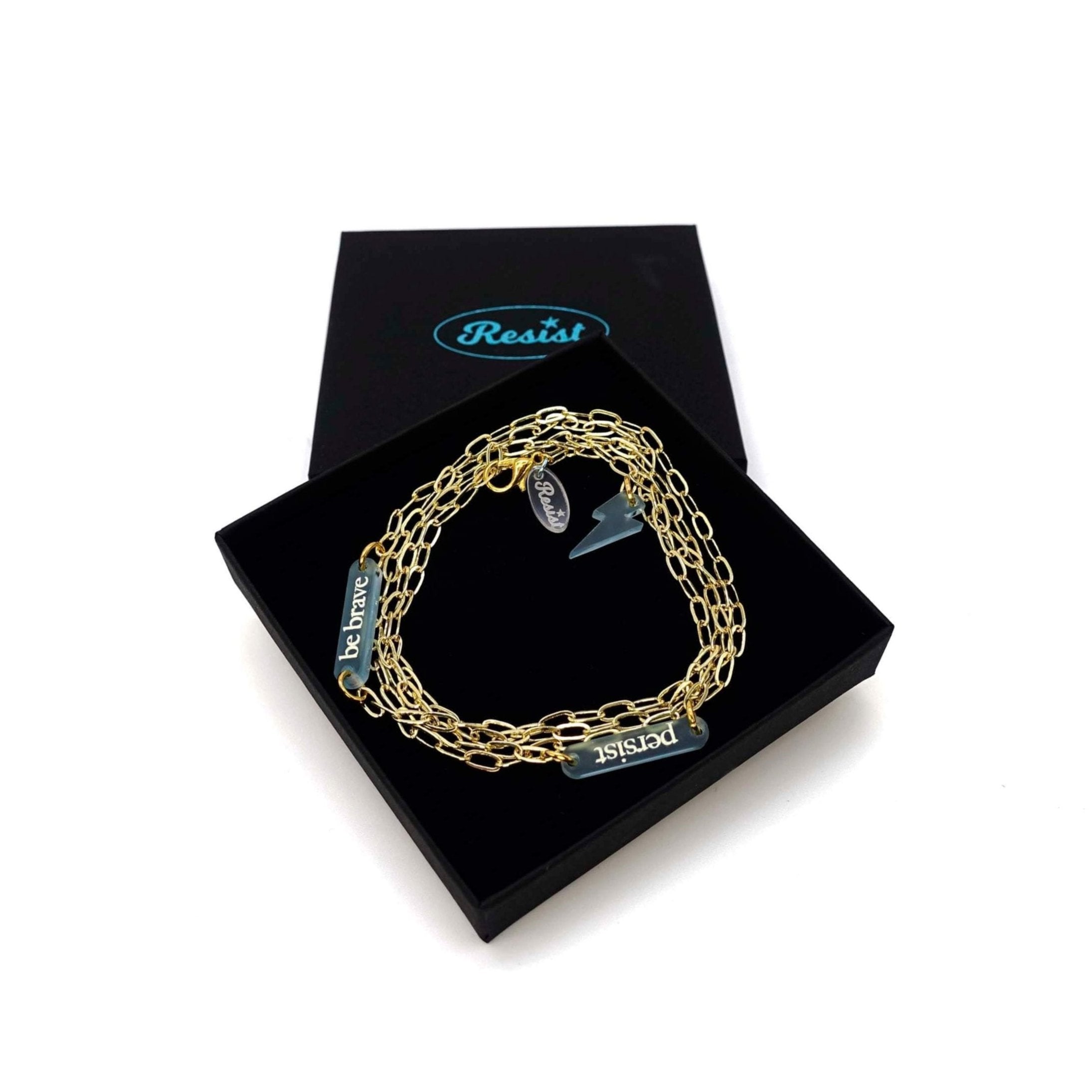 The Have a Word with Yourself design on a gold-plated paperclip chain, with the words 'persist' and 'be brave' etched in glow-in-the-dark pigment and finished with a lightning bolt charm. Shown in a Wear and Resist gift box.