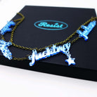 A close up of a F*ck these F*cking F*ckers necklace in sky mirror, shown on top of a large Wear and Resist gift box.