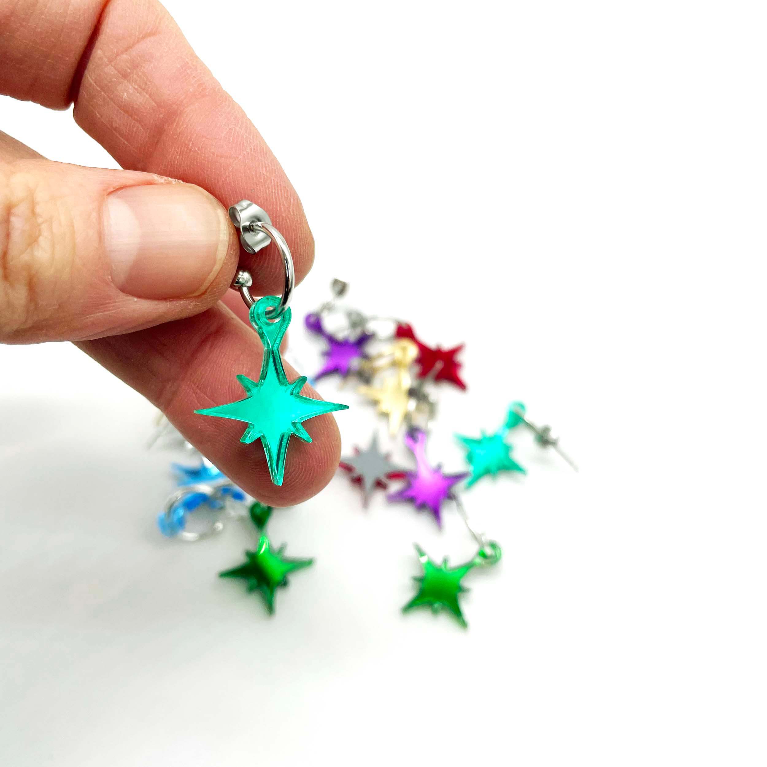 Vintage star earrings in various colours shown with my hand holding up an electric green star.