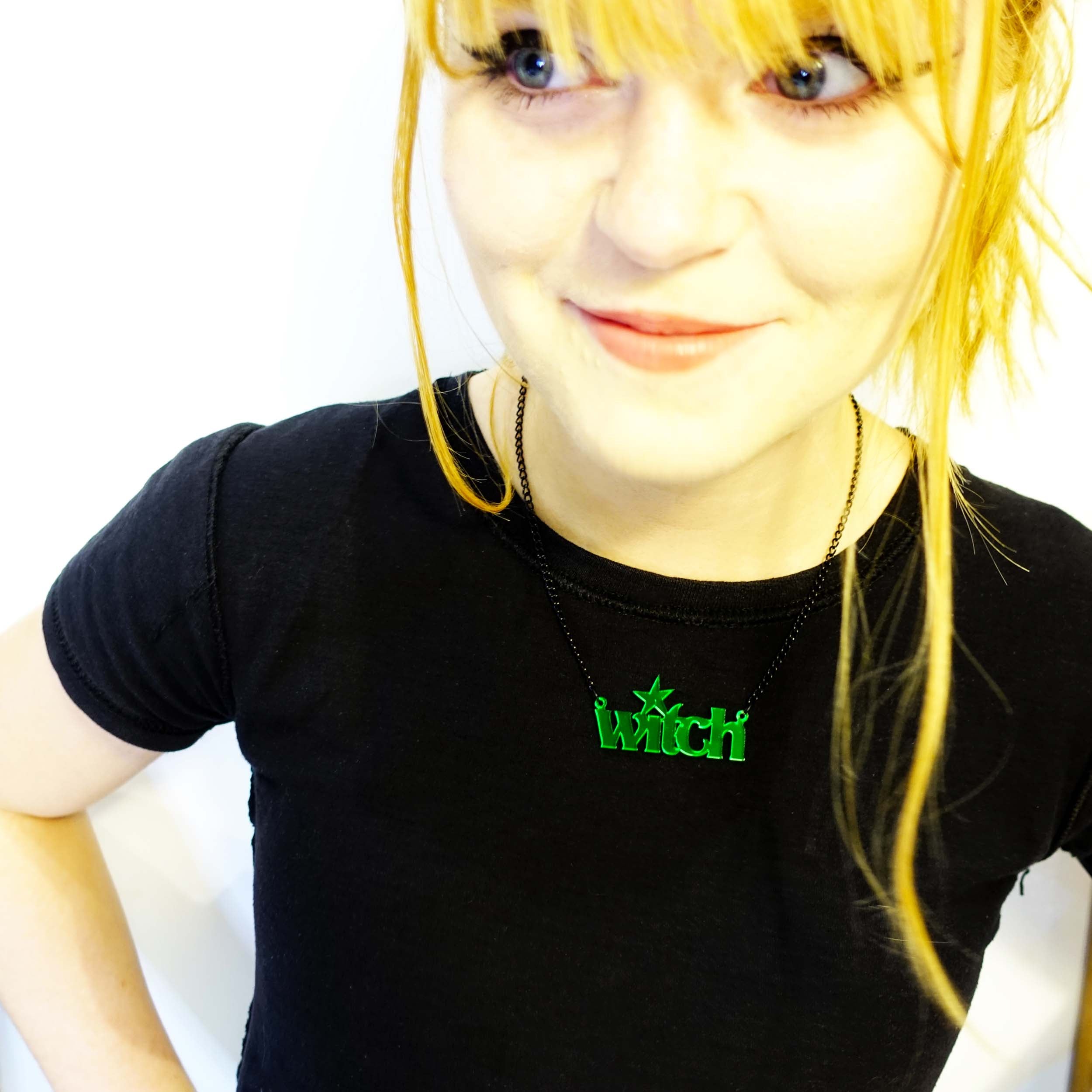 Eliza wearing envy green Witch necklace, smiling in a black t shirt.