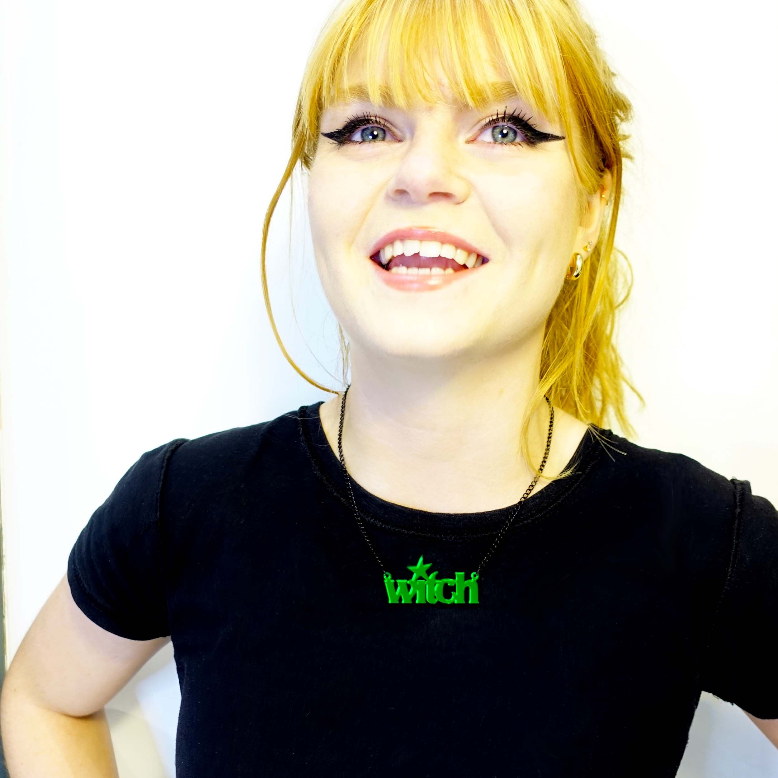 Eliza wears an envy green witch necklace, laughing at the patriarchy.