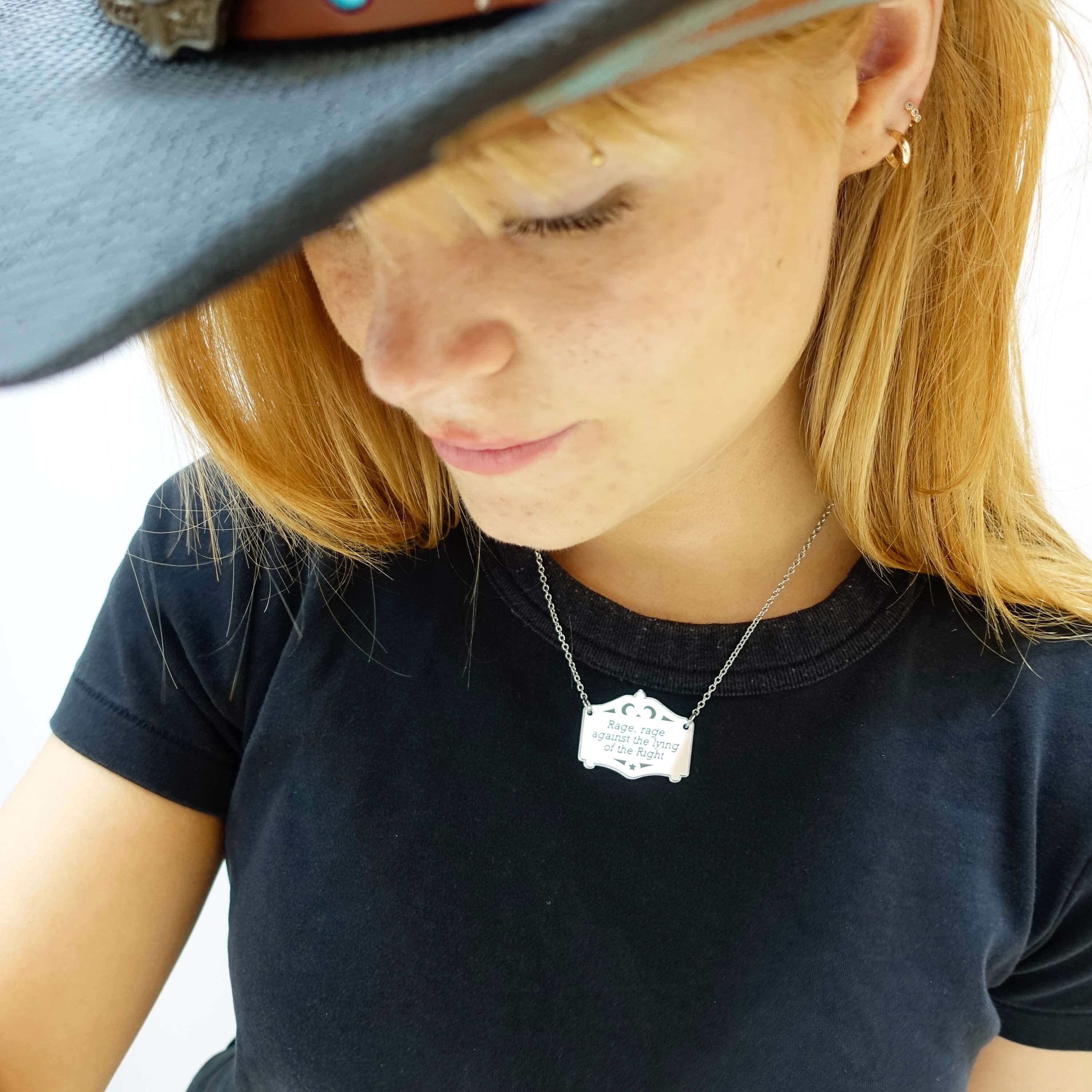 Eliza wears a Rage, rage against the lying of the right Mirror Cowboy scroll in silver on a stainless steel chain. 
