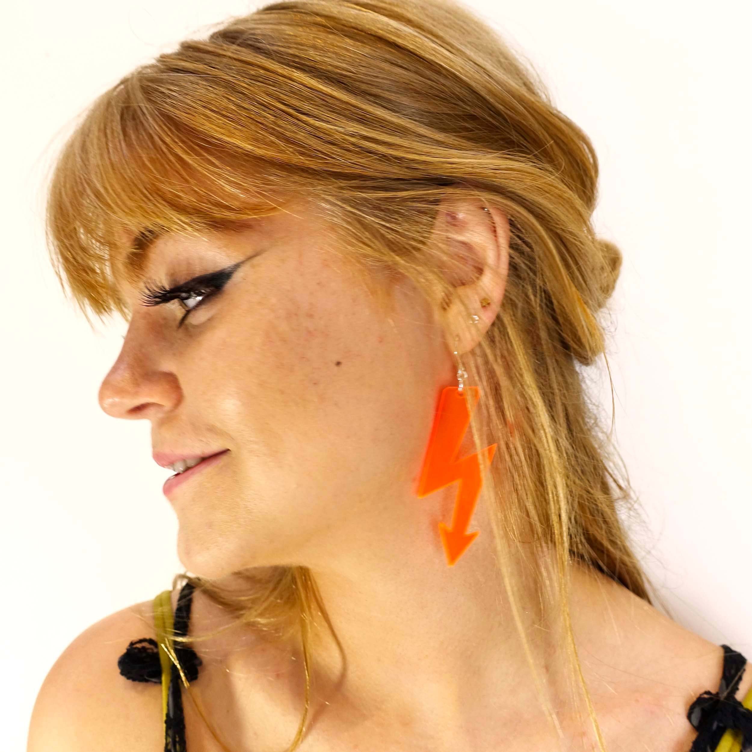 Eliza wears orange high voltage earrings.